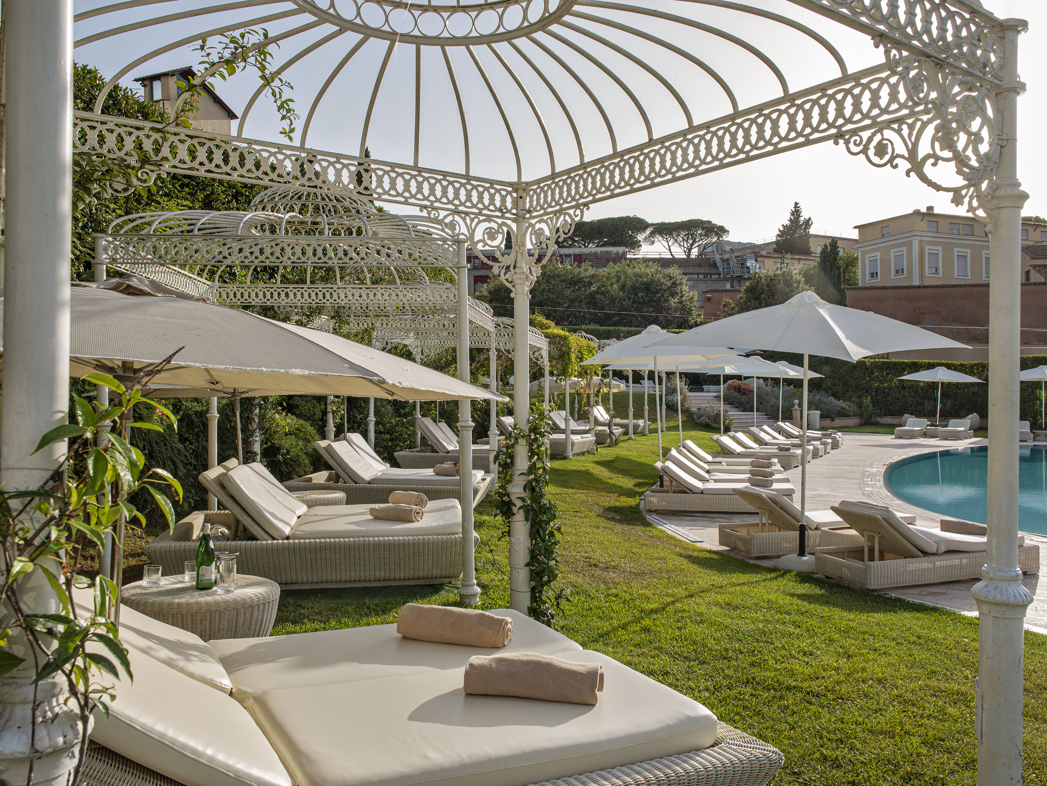 Elegant hotel pool area with white pergolas, sun loungers, and green grass.