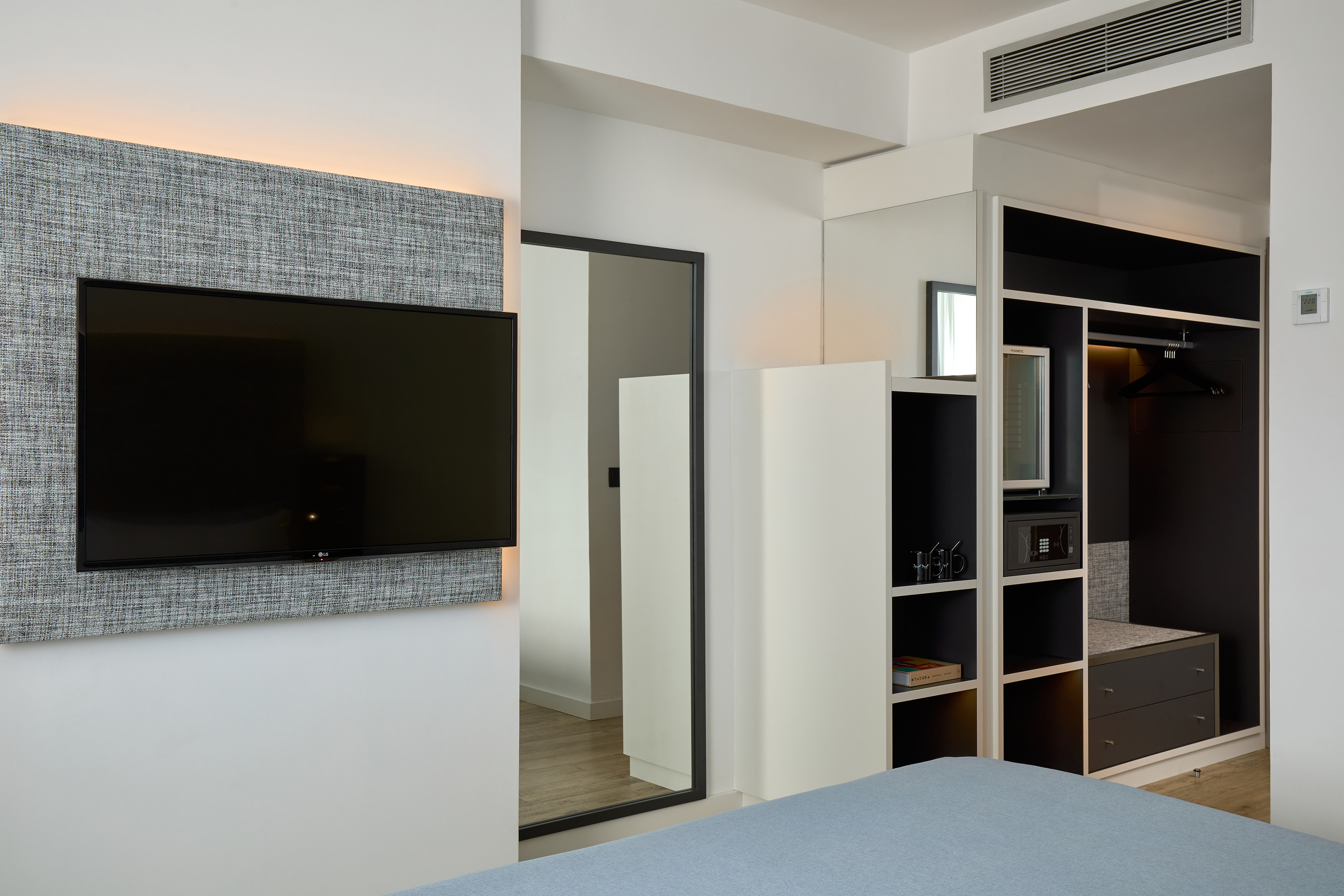 Modern hotel room with wall-mounted TV, full-length mirror, and built-in wardrobe.