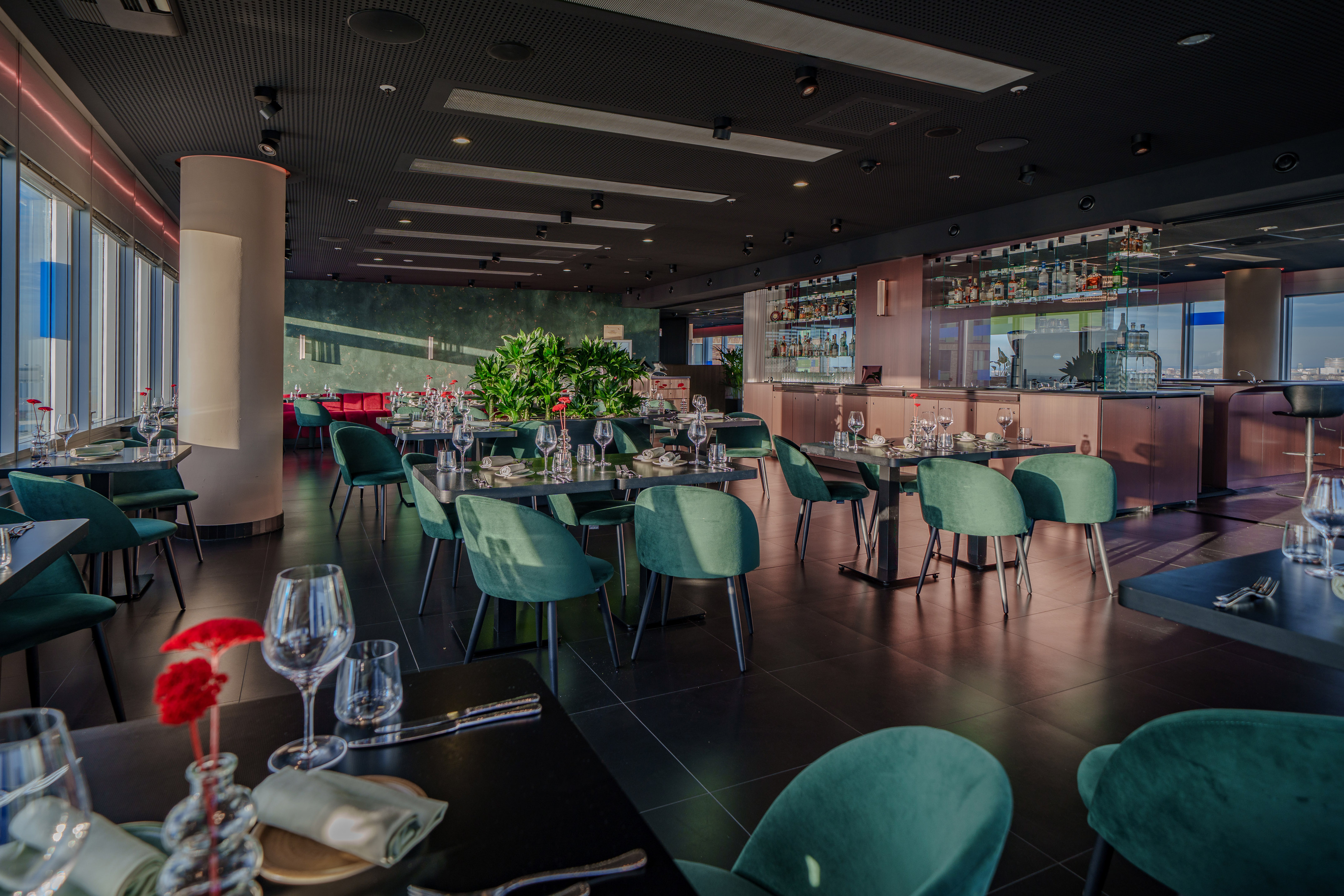 Elegant modern restaurant with green chairs, bar, and expansive city view.