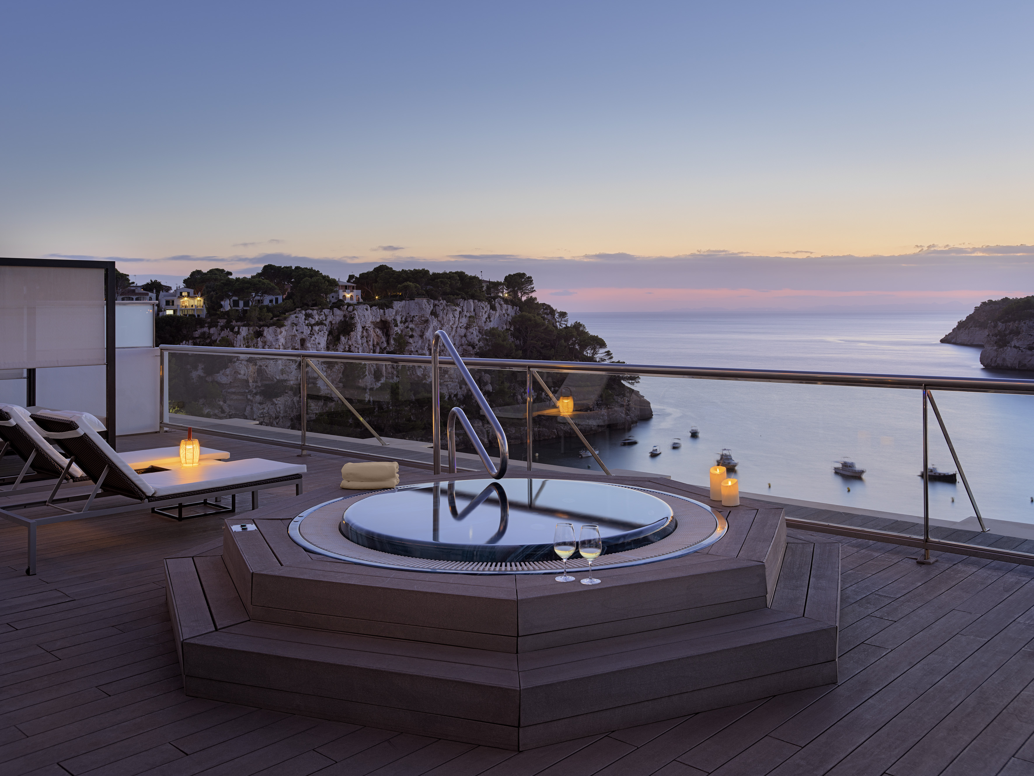 Luxury terrace hot tub with sunset ocean view and wine glasses.