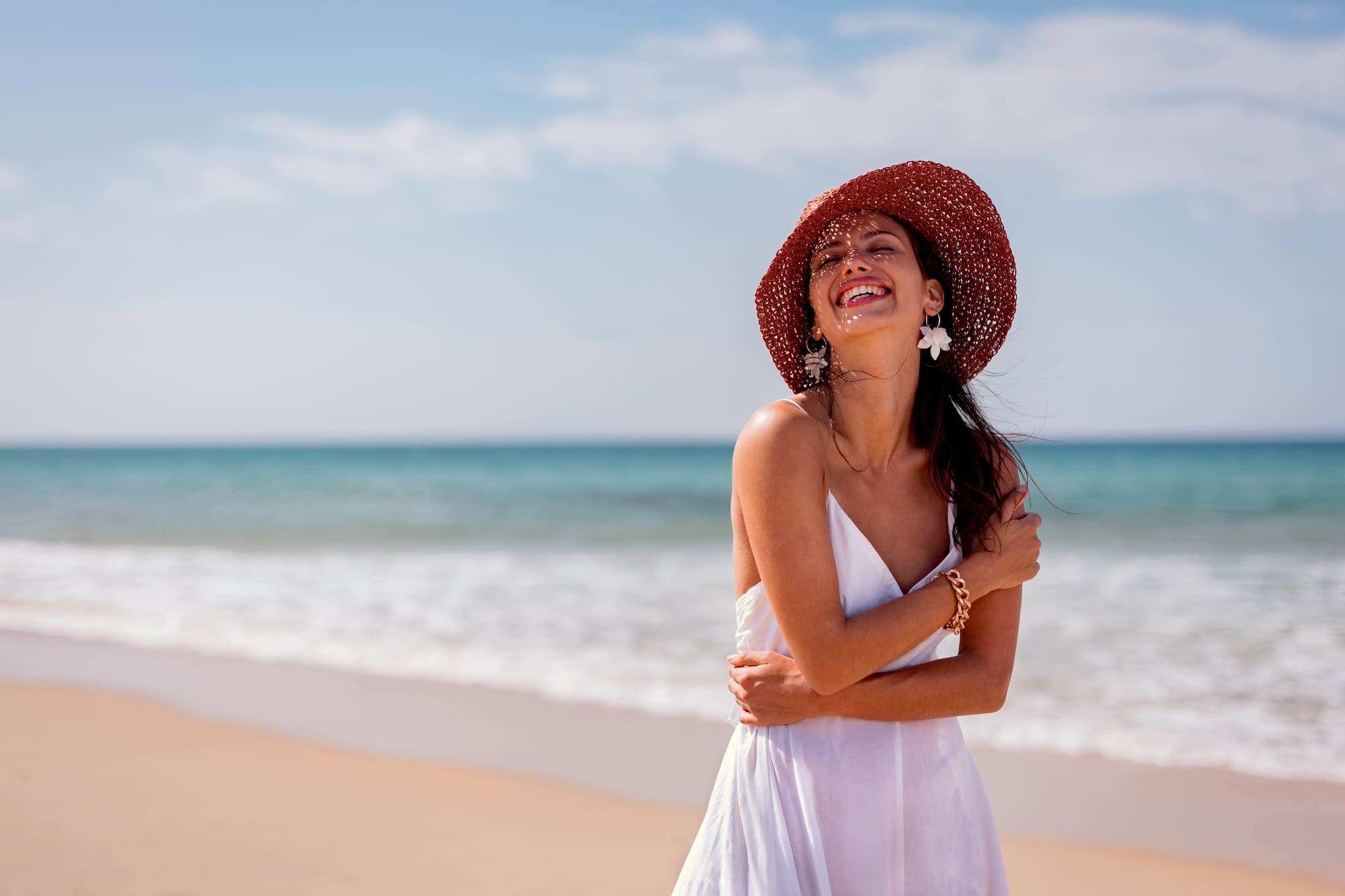 a woman in a white dress and hat on a beach