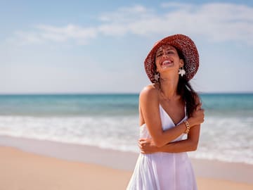 a woman in a white dress and hat on a beach