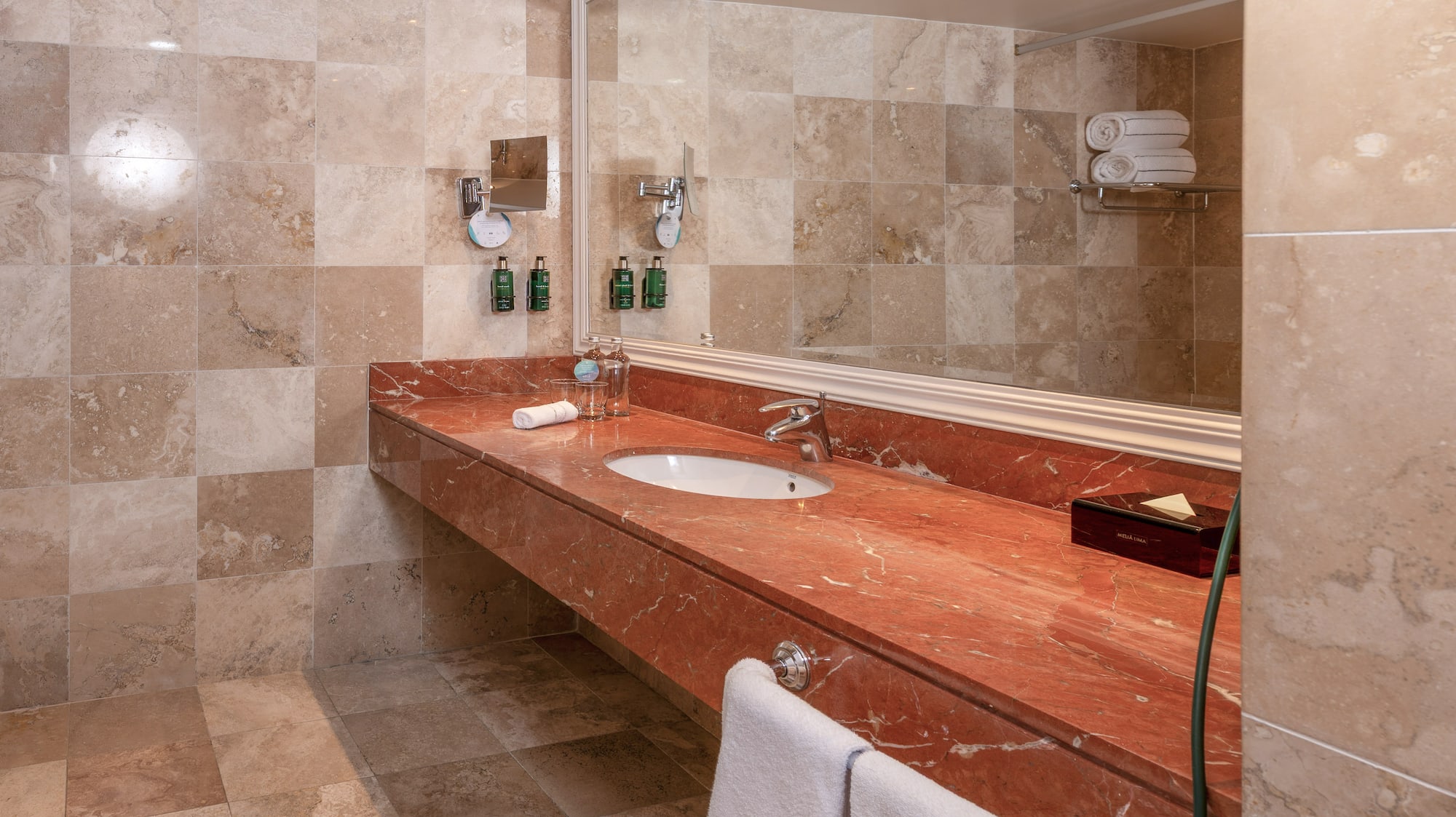 Baño moderno con lavabo, tocador de mármol rojo y azulejos beige.