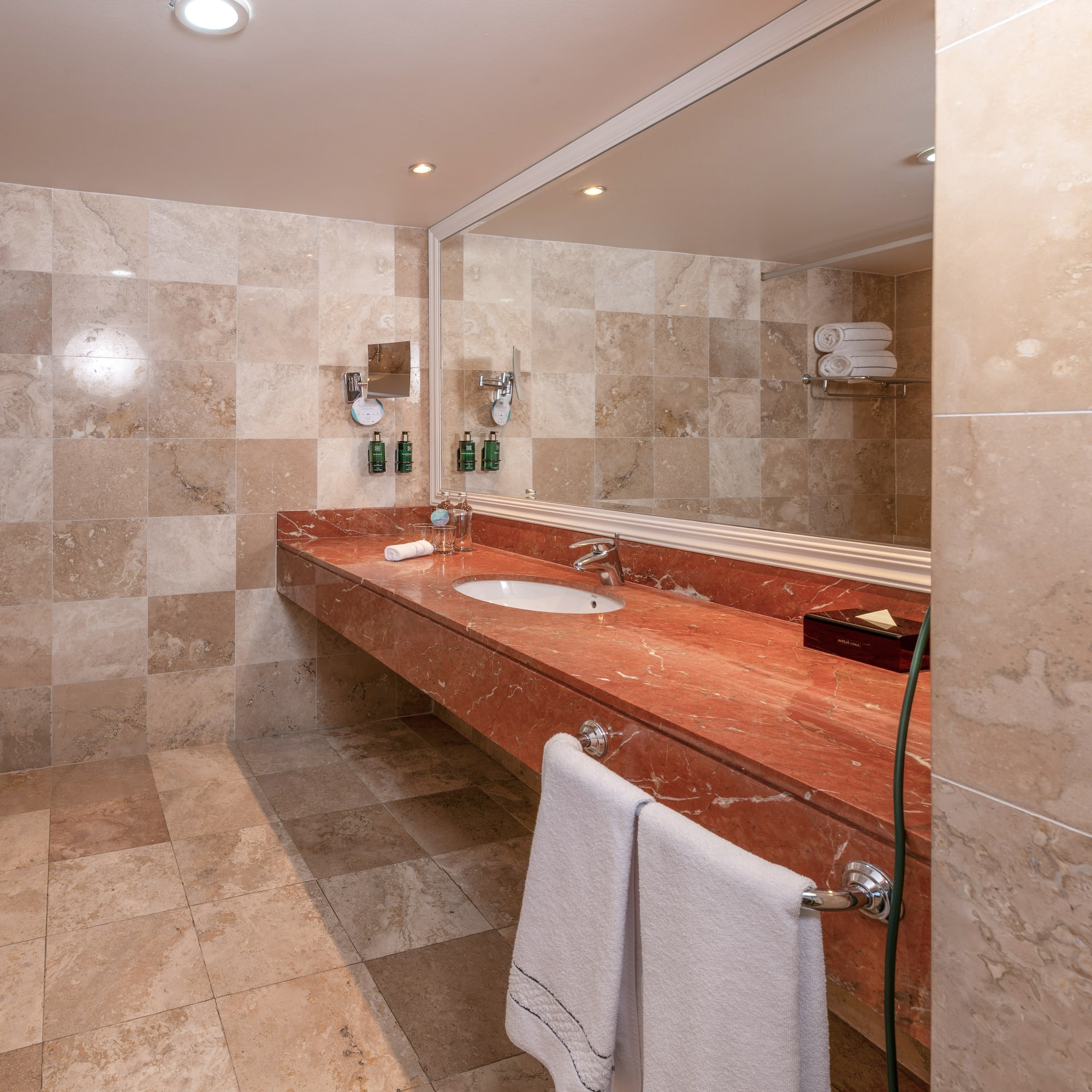 Baño moderno con lavabo, tocador de mármol rojo y azulejos beige.
