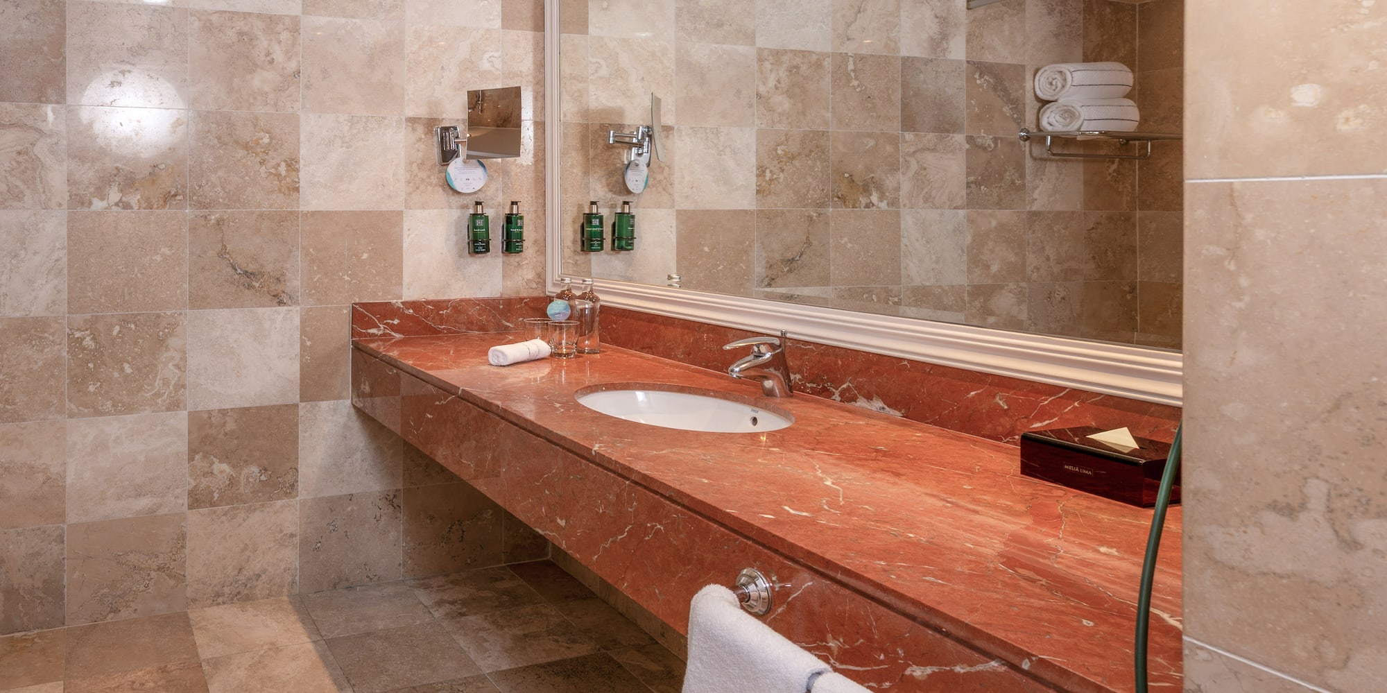 Baño moderno con lavabo, tocador de mármol rojo y azulejos beige.