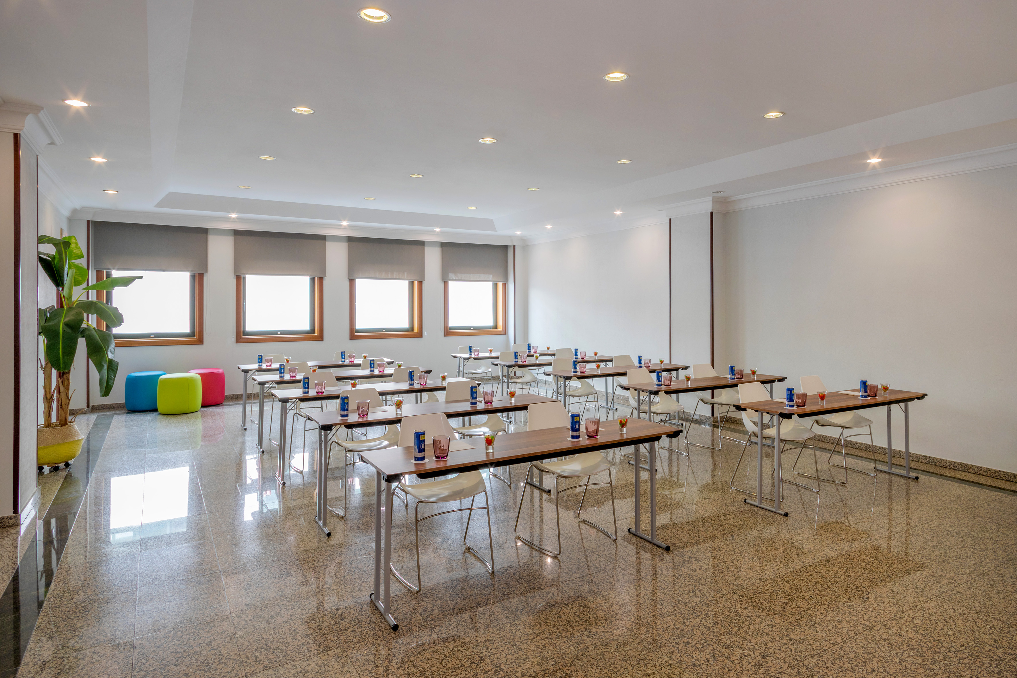 Bright conference room with rows of tables, chairs, and large windows.
