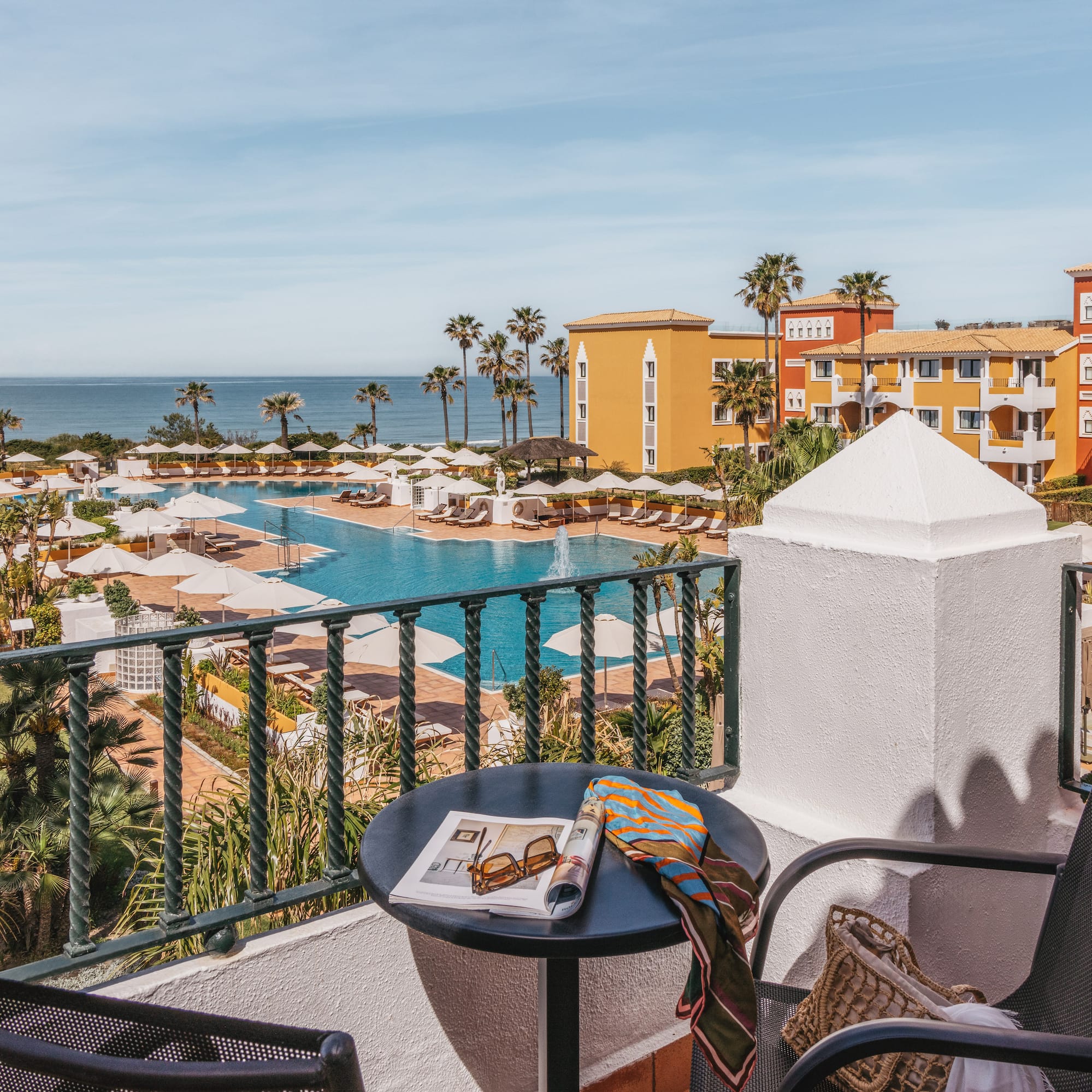 Balcony view of a colorful luxury resort with pools, palm trees, and ocean.