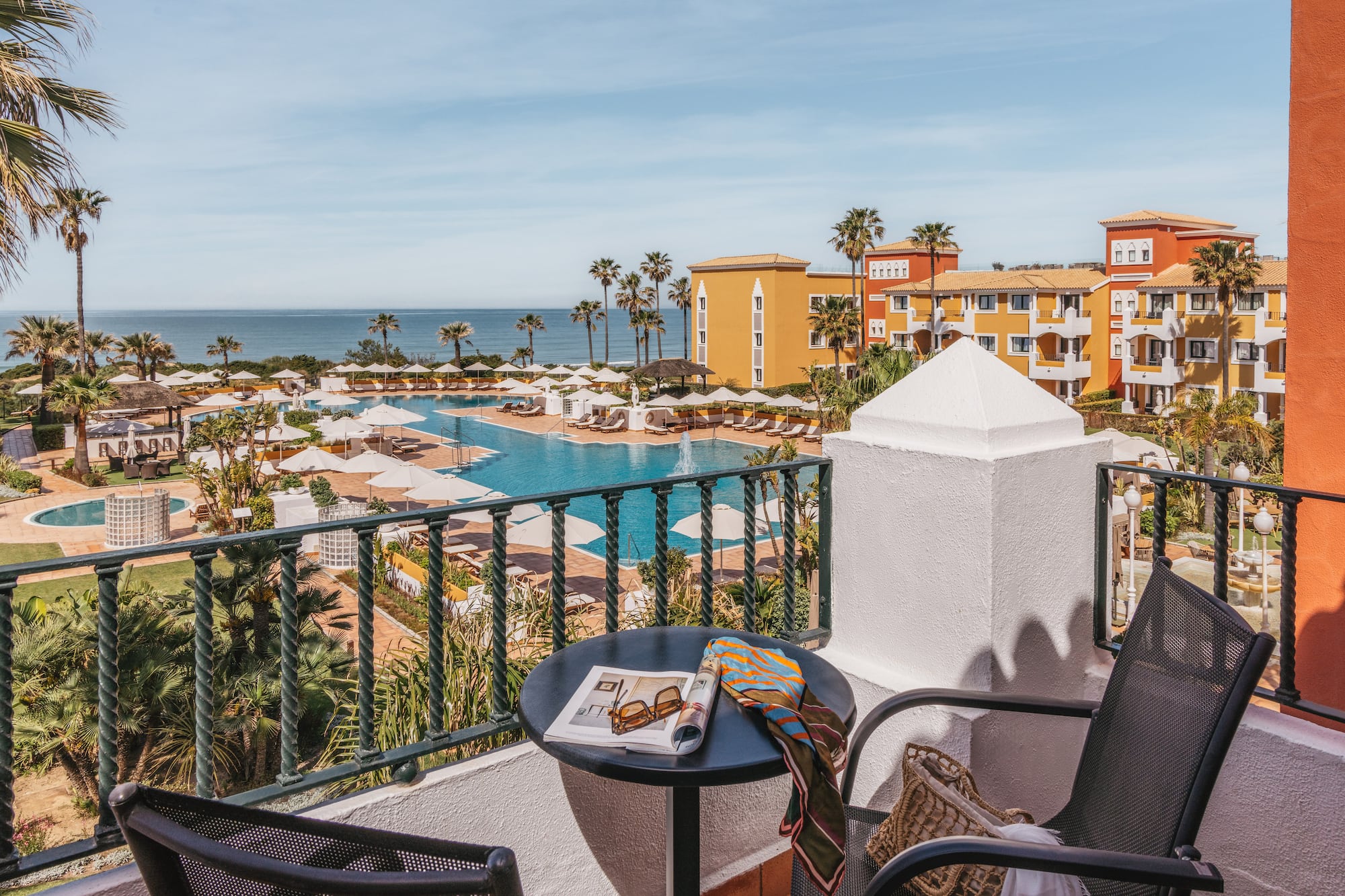 Balcony view of a colorful luxury resort with pools, palm trees, and ocean.