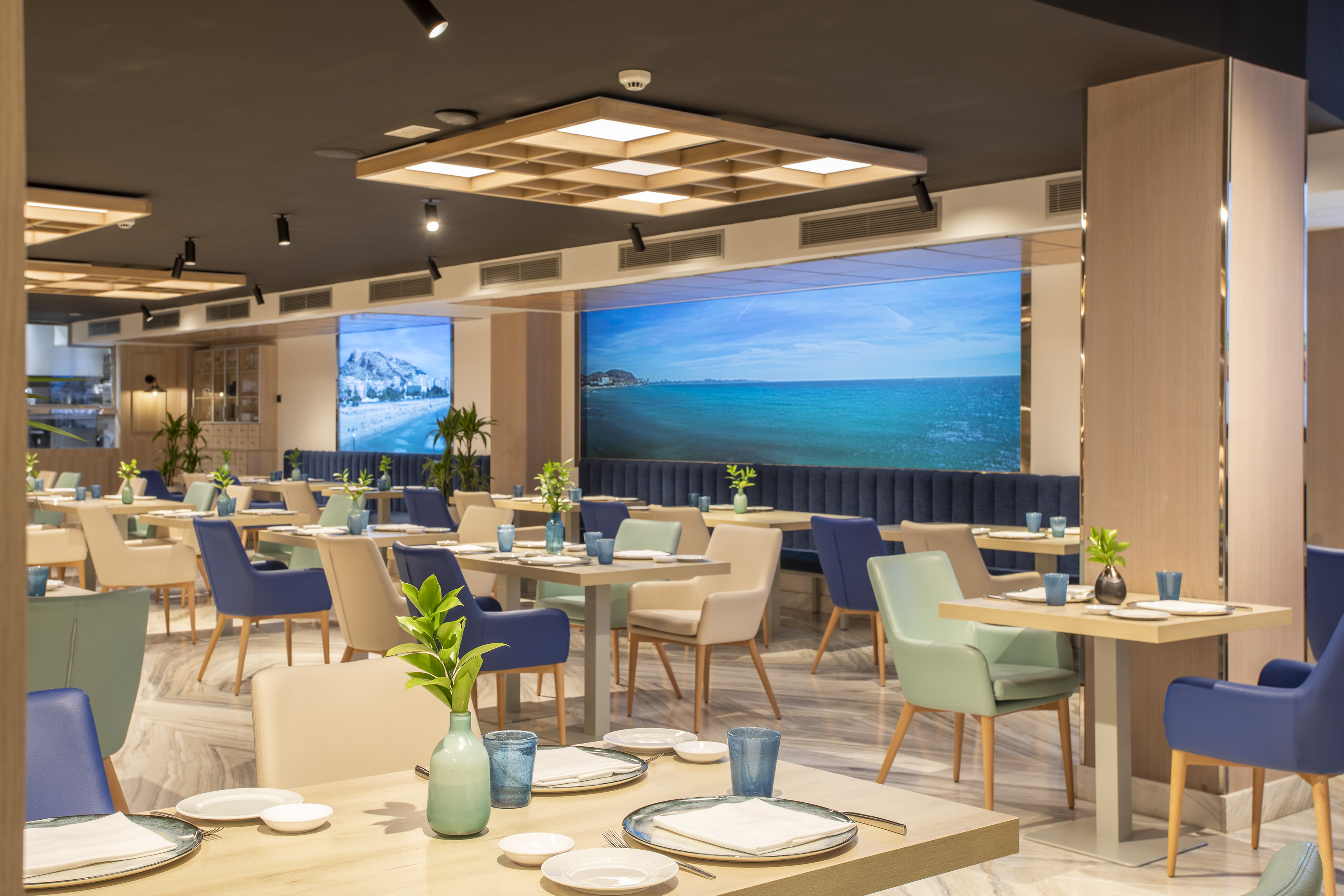 Modern restaurant with colorful seating, wooden tables, and digital ocean views.