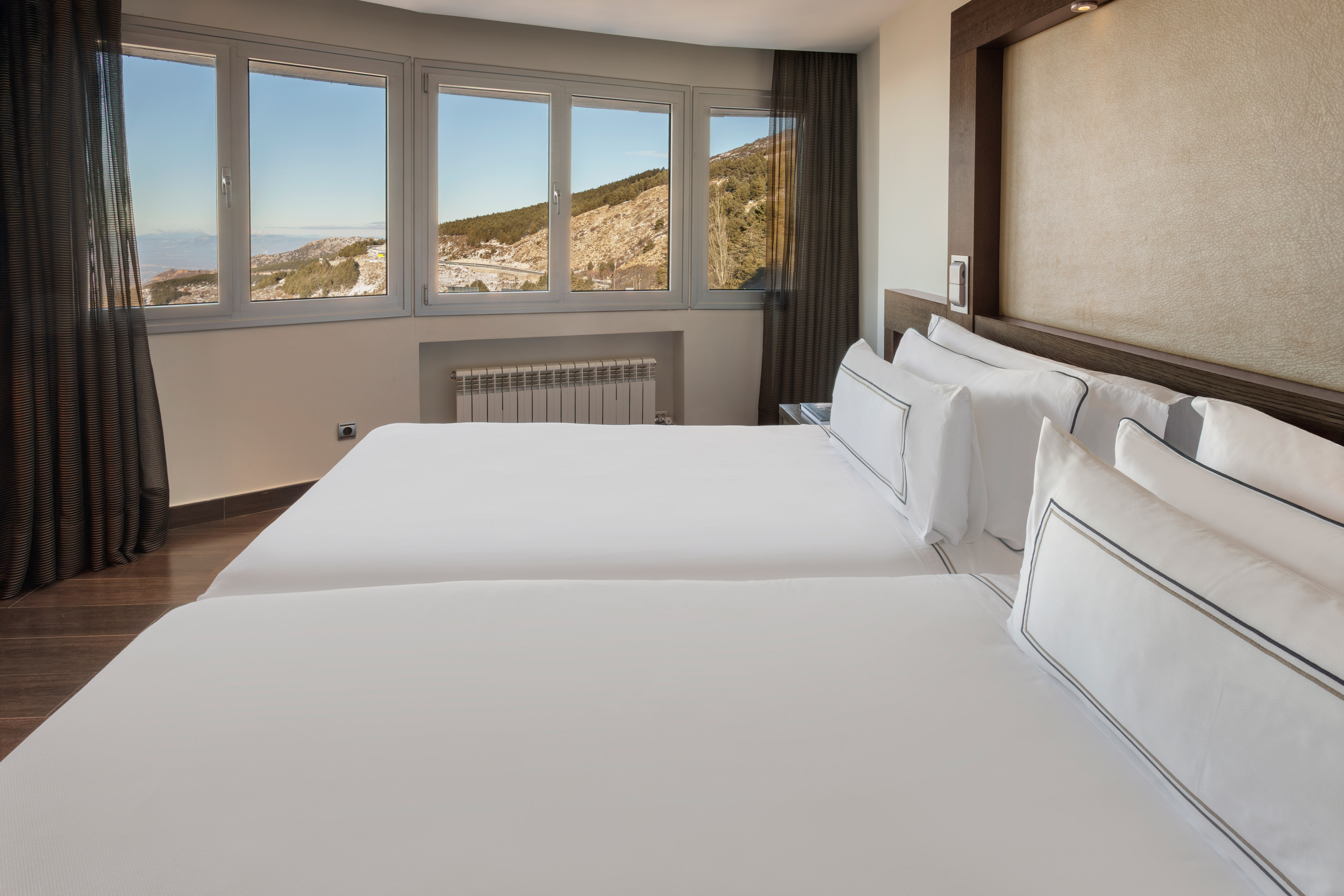 Hotel room with two single beds, white bedding, and mountain view from large windows.