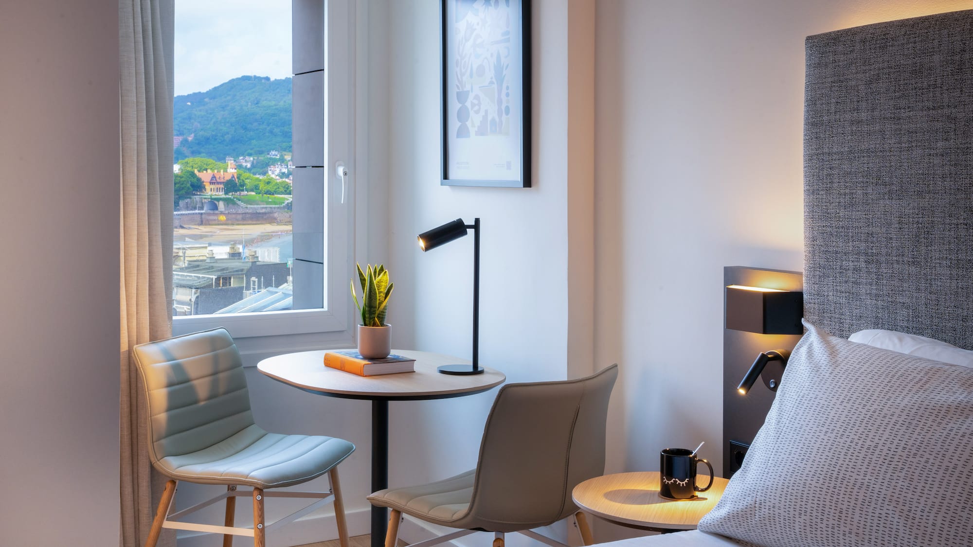 Habitación moderna de hotel con vistas al mar, montaña, cama y mesa.