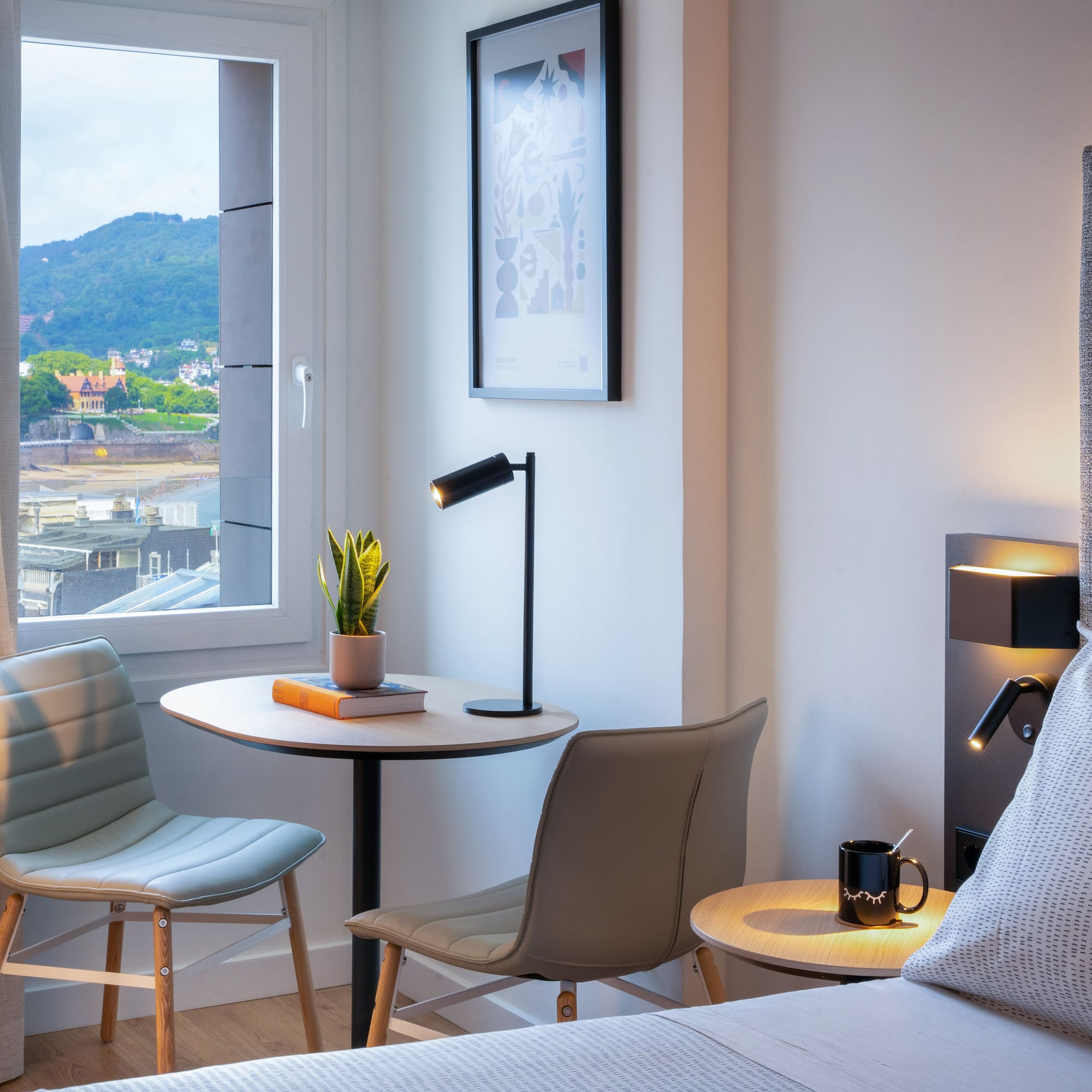 Habitación moderna de hotel con vistas al mar, montaña, cama y mesa.