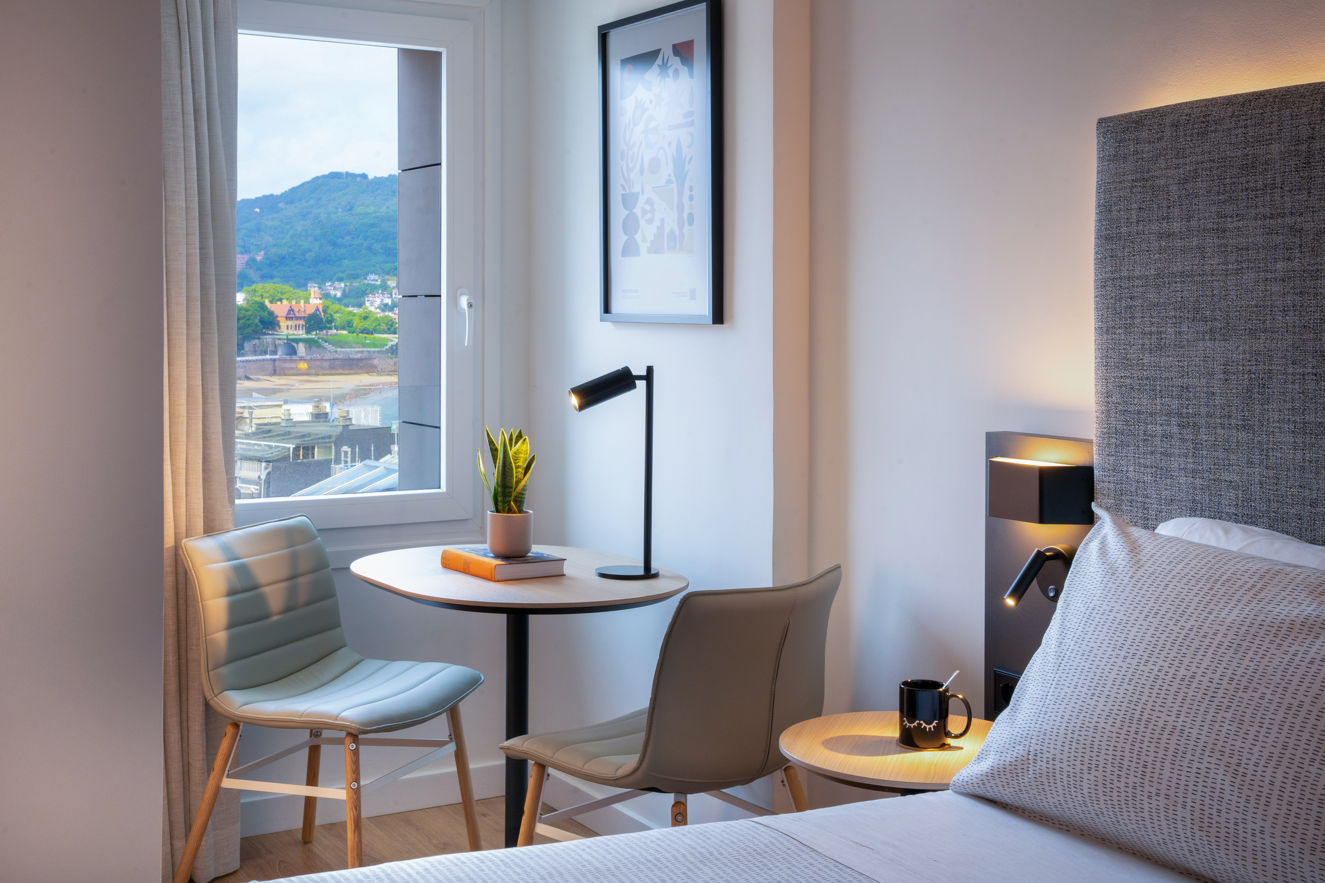 Habitación moderna de hotel con vistas al mar, montaña, cama y mesa.