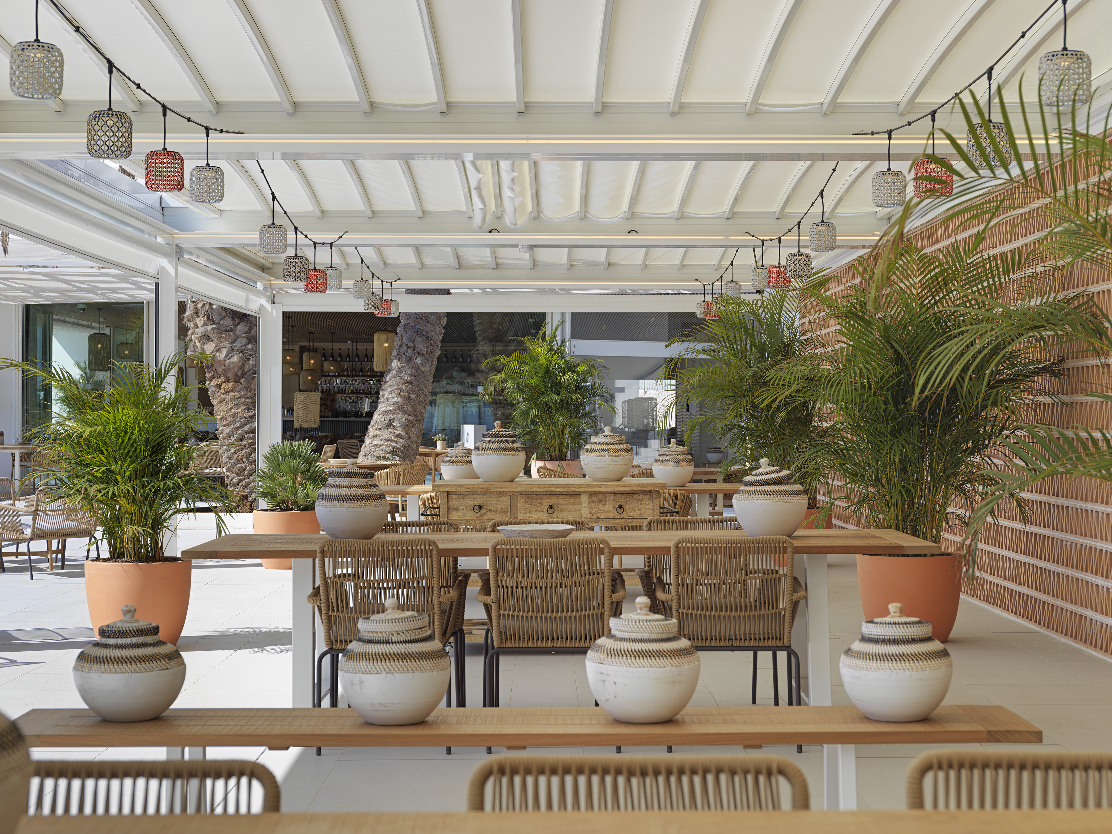Outdoor resort dining with rattan chairs, palm plants, and string lights.