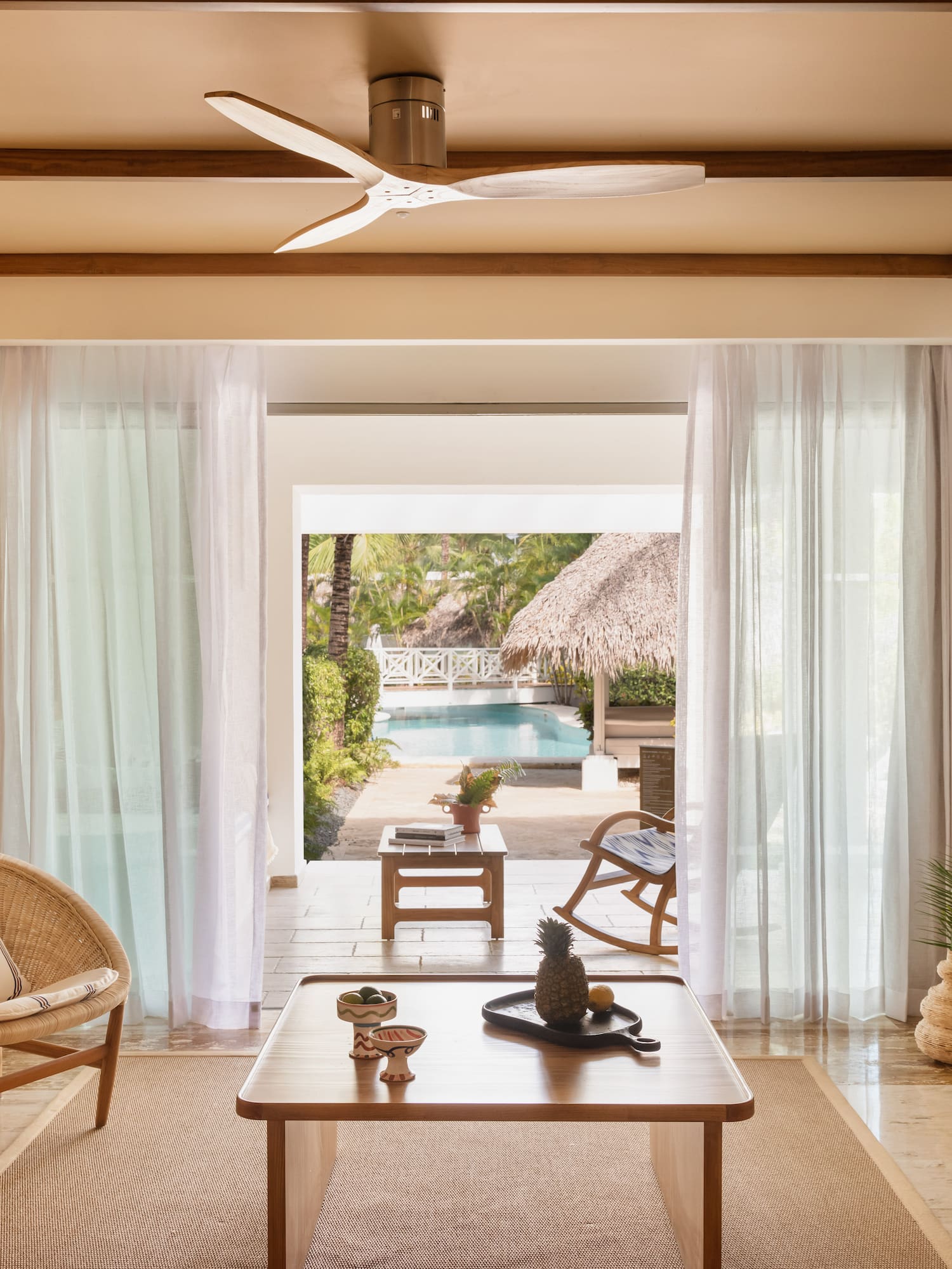 Tropical living room with wicker chairs, pool view, and ceiling fan.
