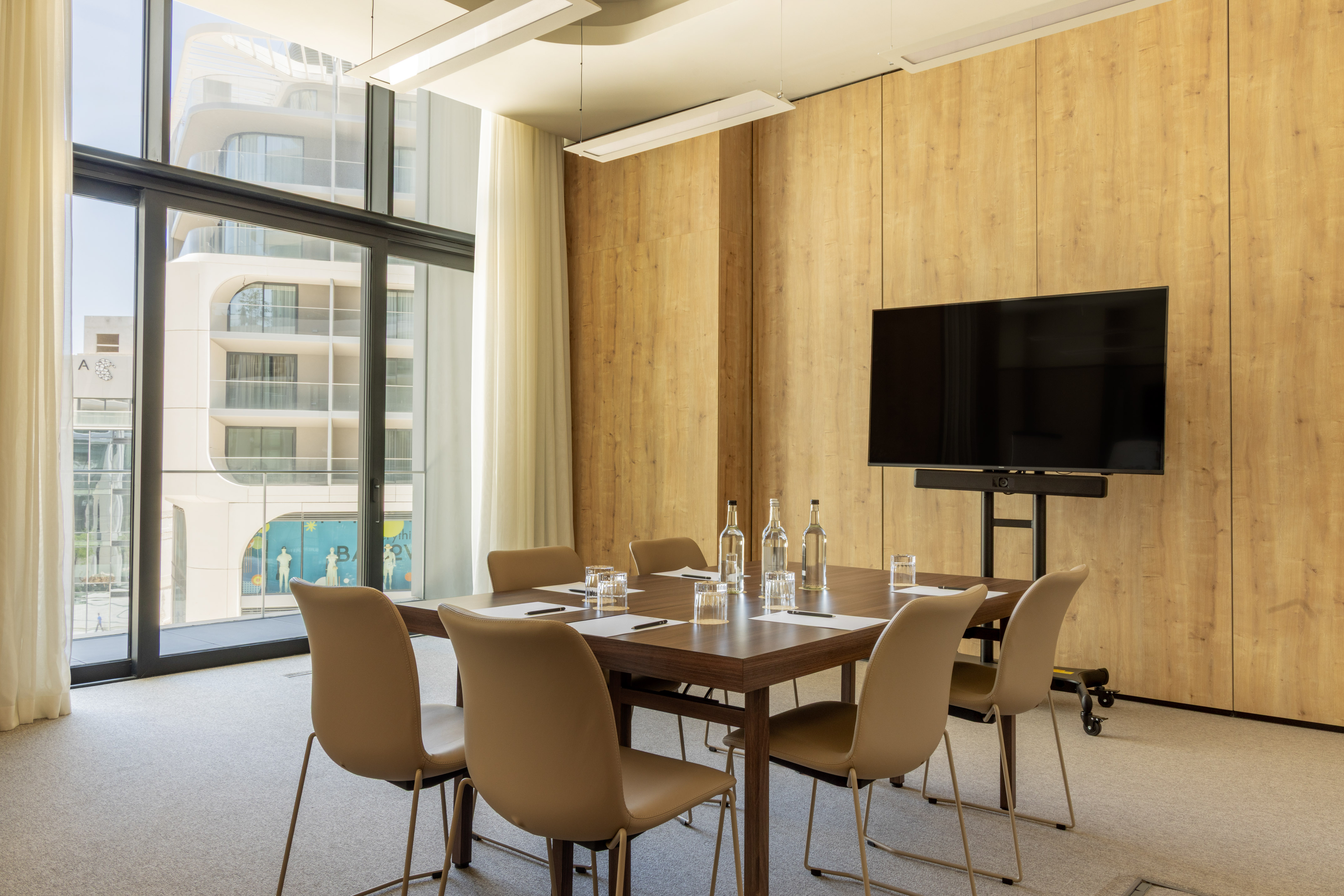 Contemporary meeting room with wood table, chairs, screen, and window.
