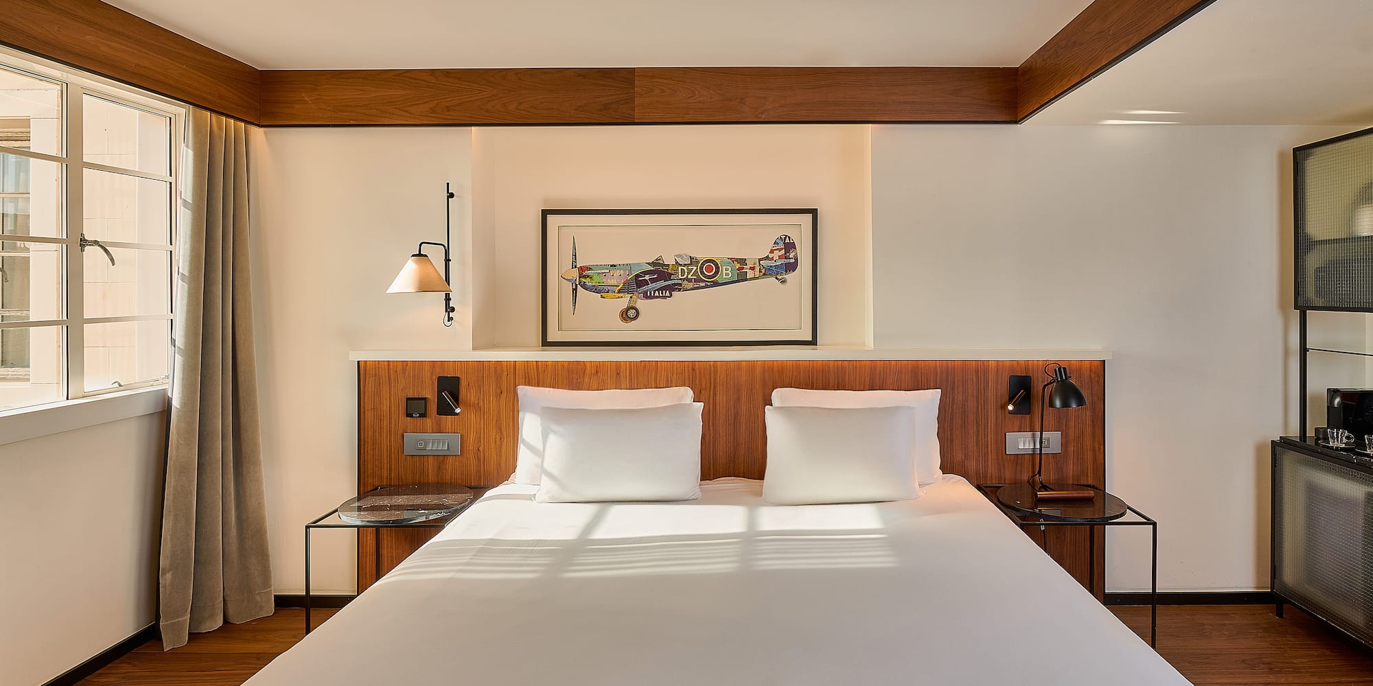 Modern hotel bedroom, king bed, wood accents, and vintage airplane artwork.