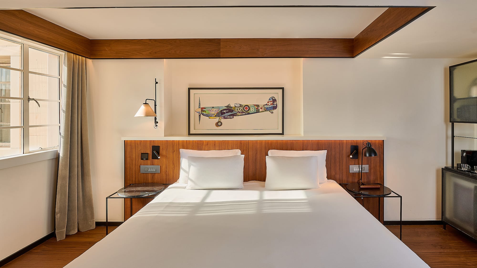 Boutique hotel room with white bed, wooden headboard, and framed airplane art.