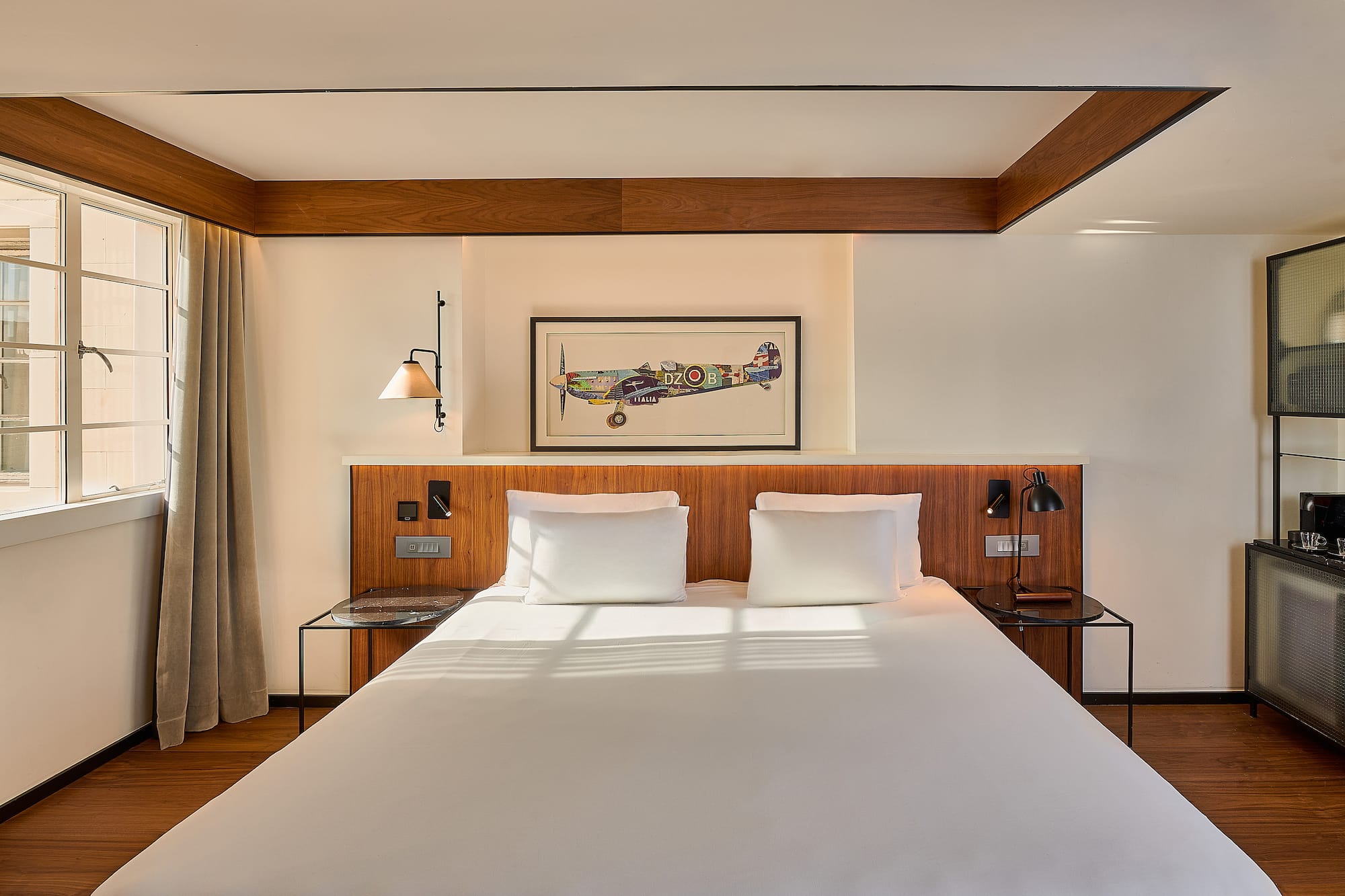 Boutique hotel room with white bed, wooden headboard, and framed airplane art.