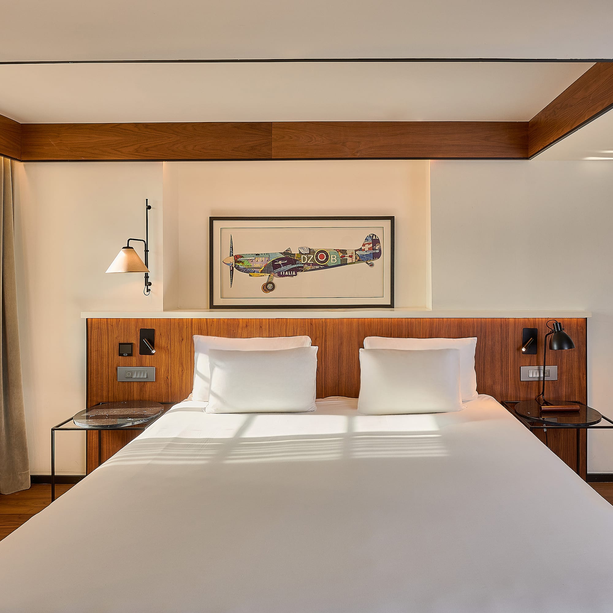 Boutique hotel room with white bed, wooden headboard, and framed airplane art.