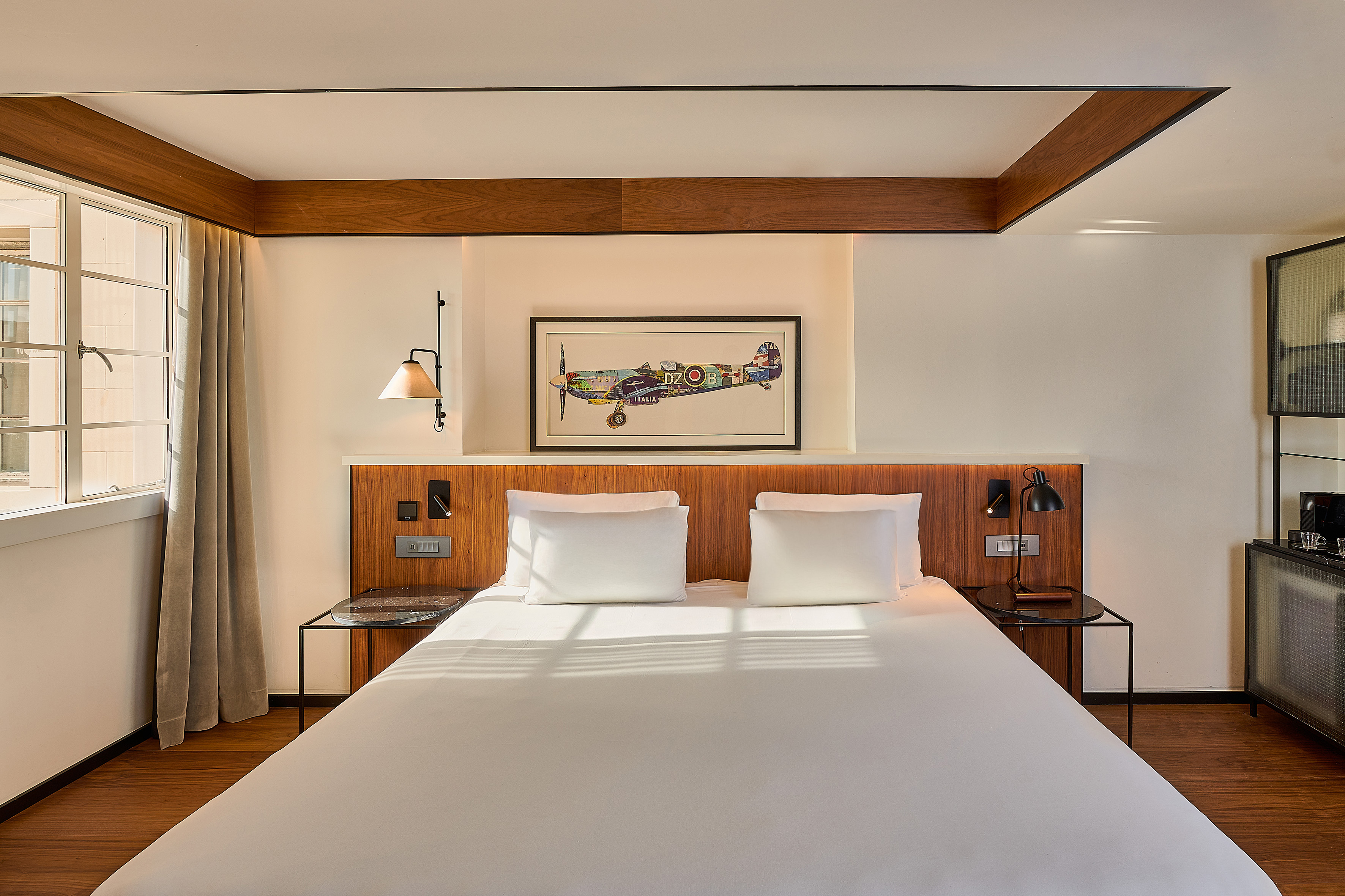 Boutique hotel room with white bed, wooden headboard, and framed airplane art.