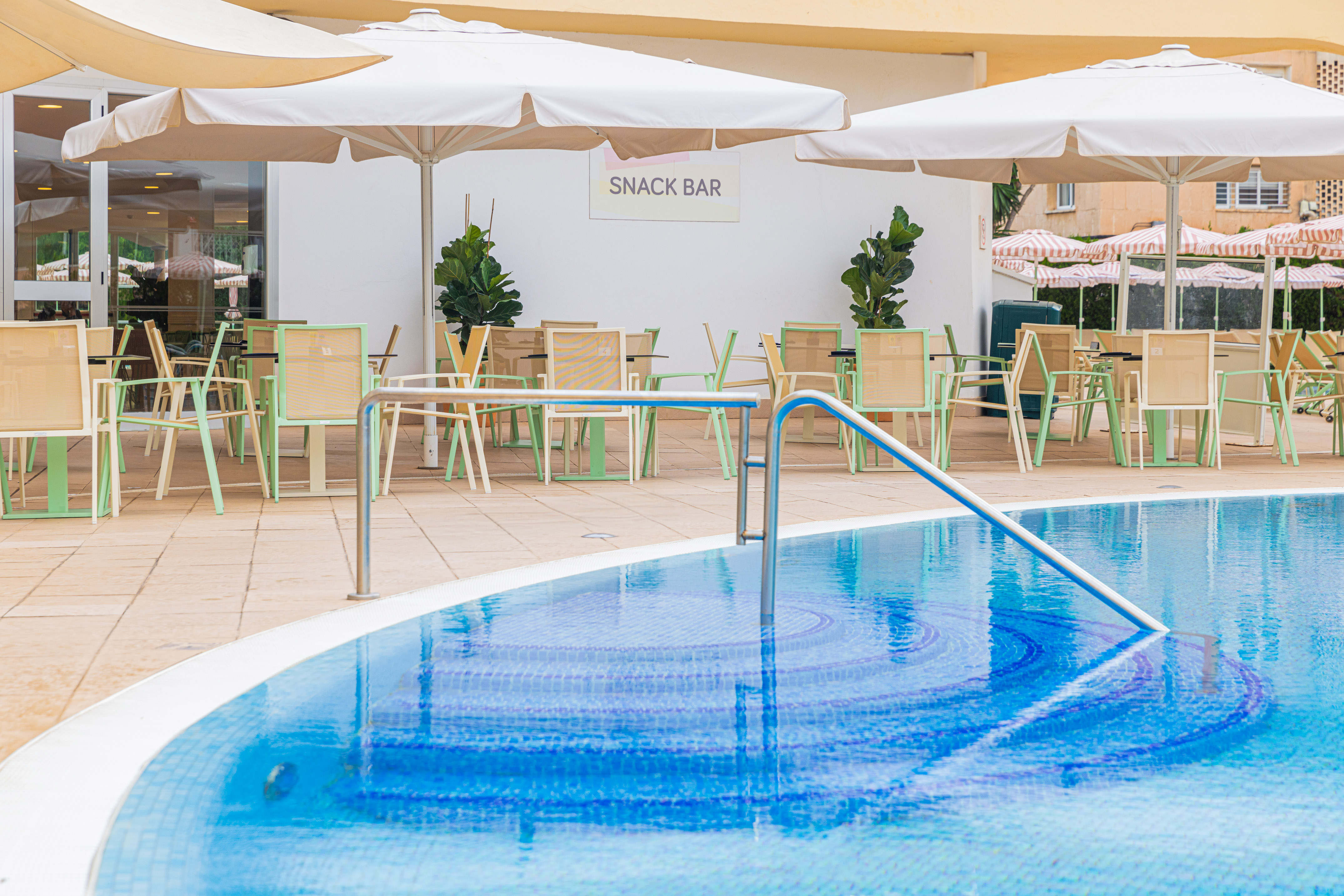 Resort swimming pool with outdoor snack bar, tables, and white umbrellas.