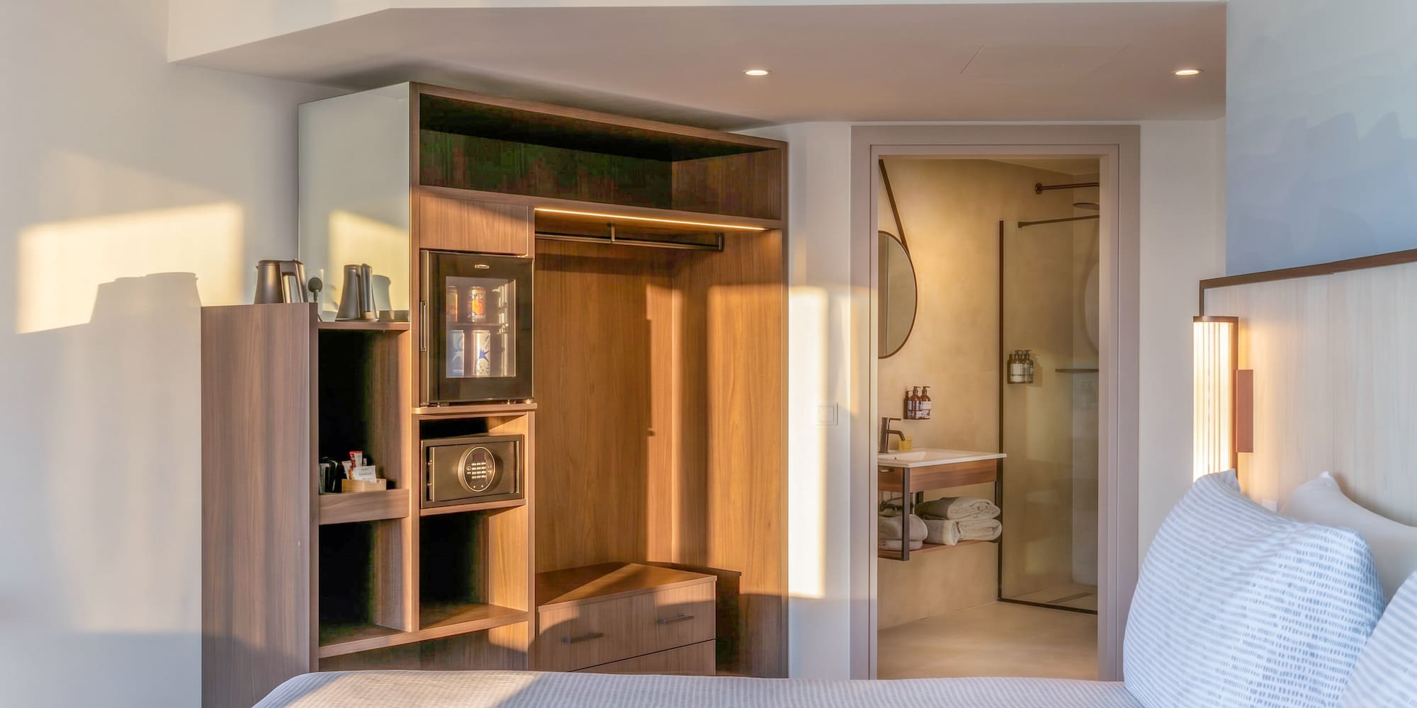 Modern hotel bedroom with bed, integrated closet, mini-bar, and bathroom.