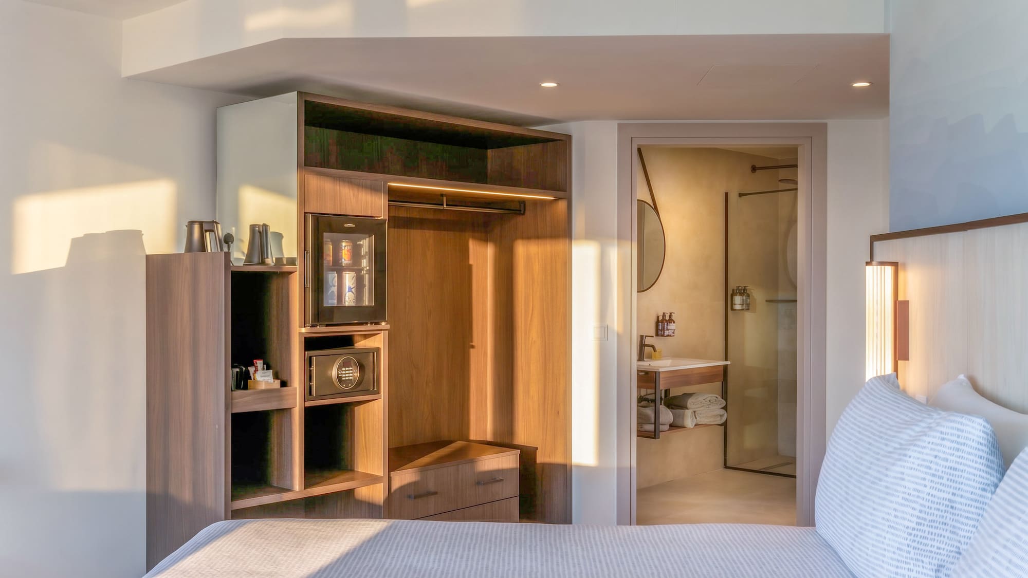 Modern hotel room with bed, wooden wardrobe, mini-bar, and ensuite bathroom.