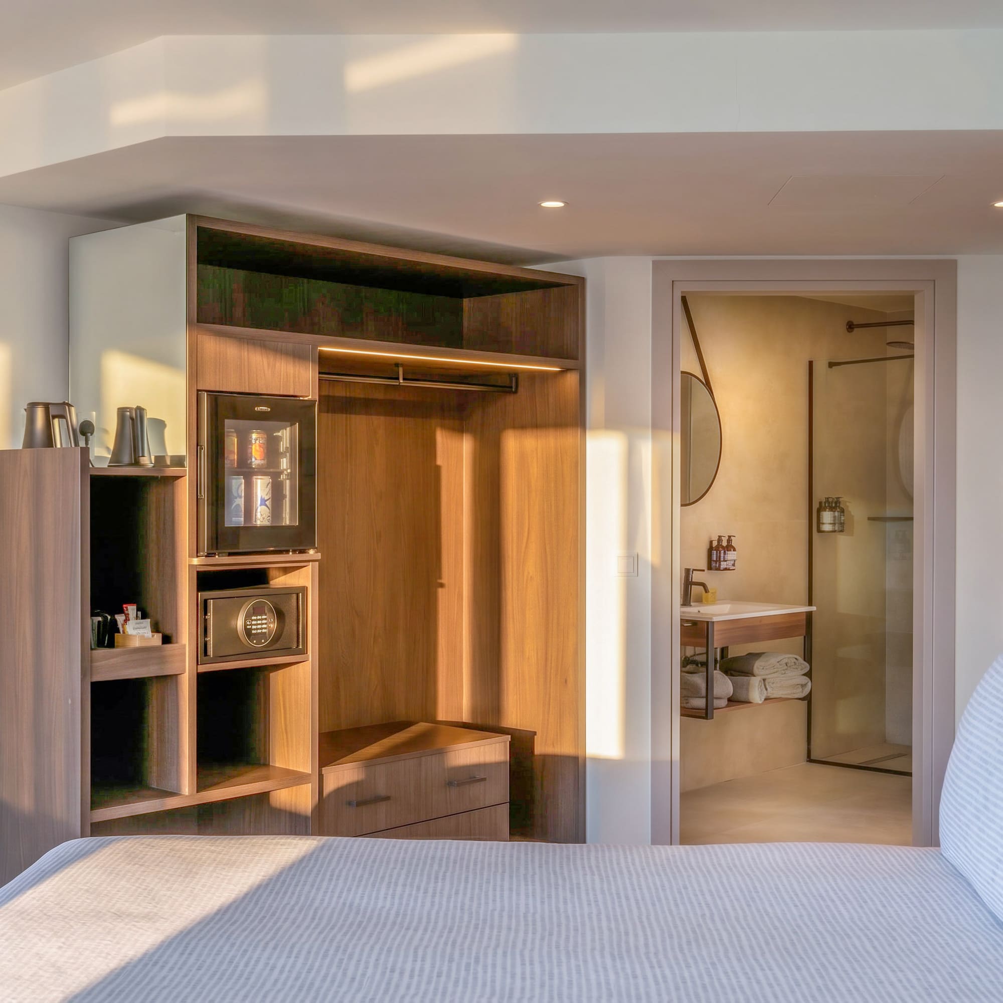 Modern hotel bedroom with bed, integrated closet, mini-bar, and bathroom.