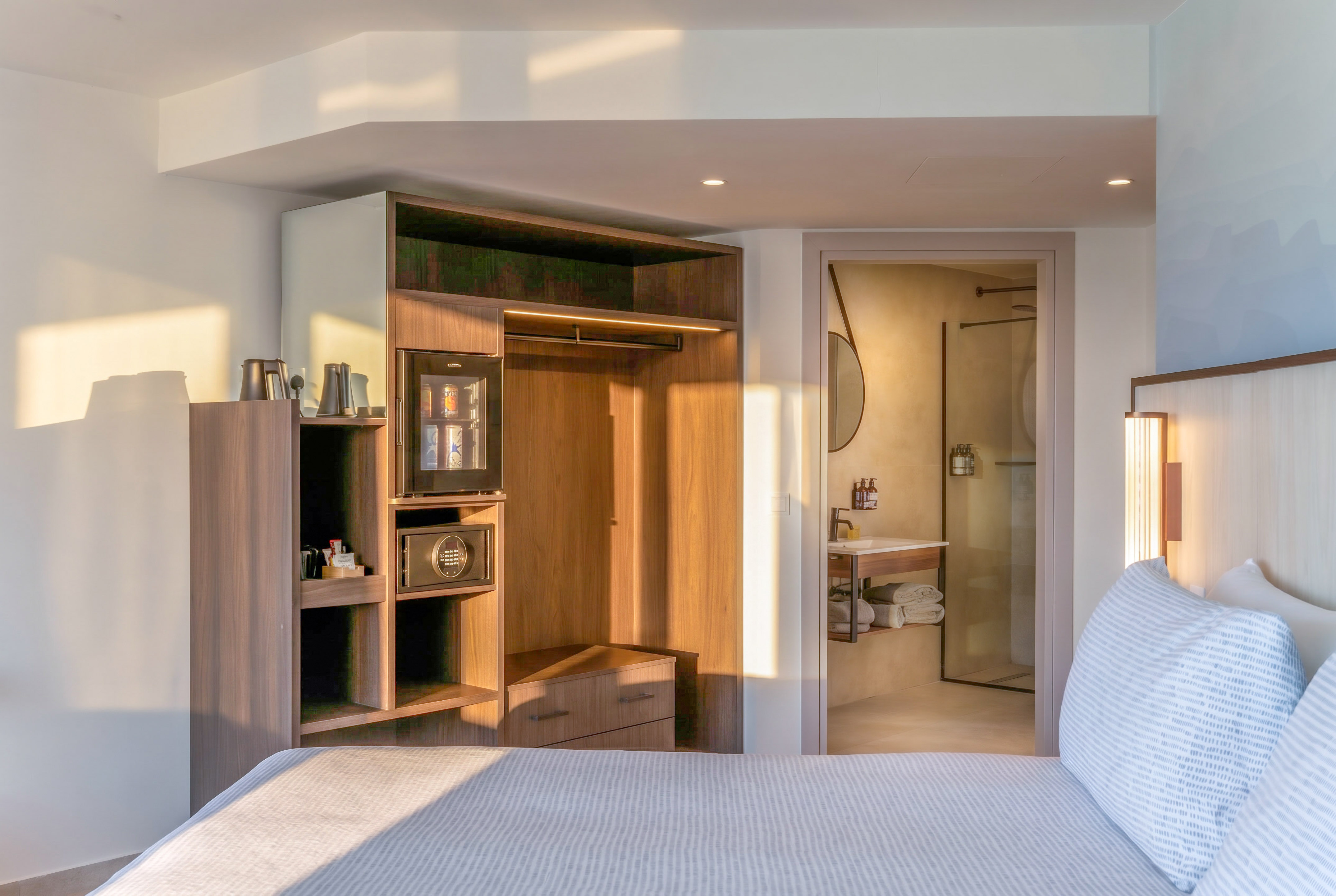 Modern hotel bedroom with bed, integrated closet, mini-bar, and bathroom.