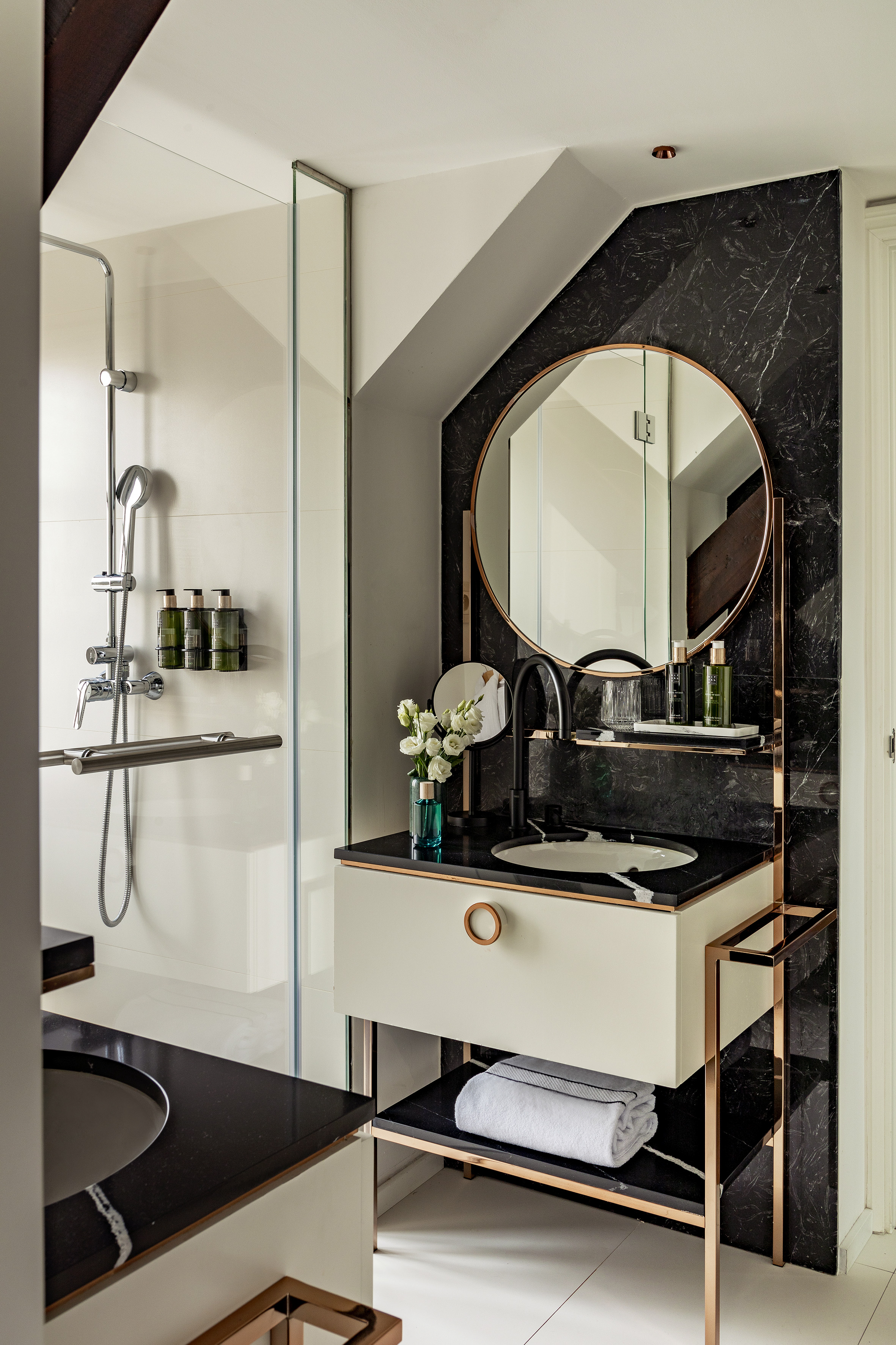 Modern bathroom with black marble vanity, copper-framed mirror, and glass shower.