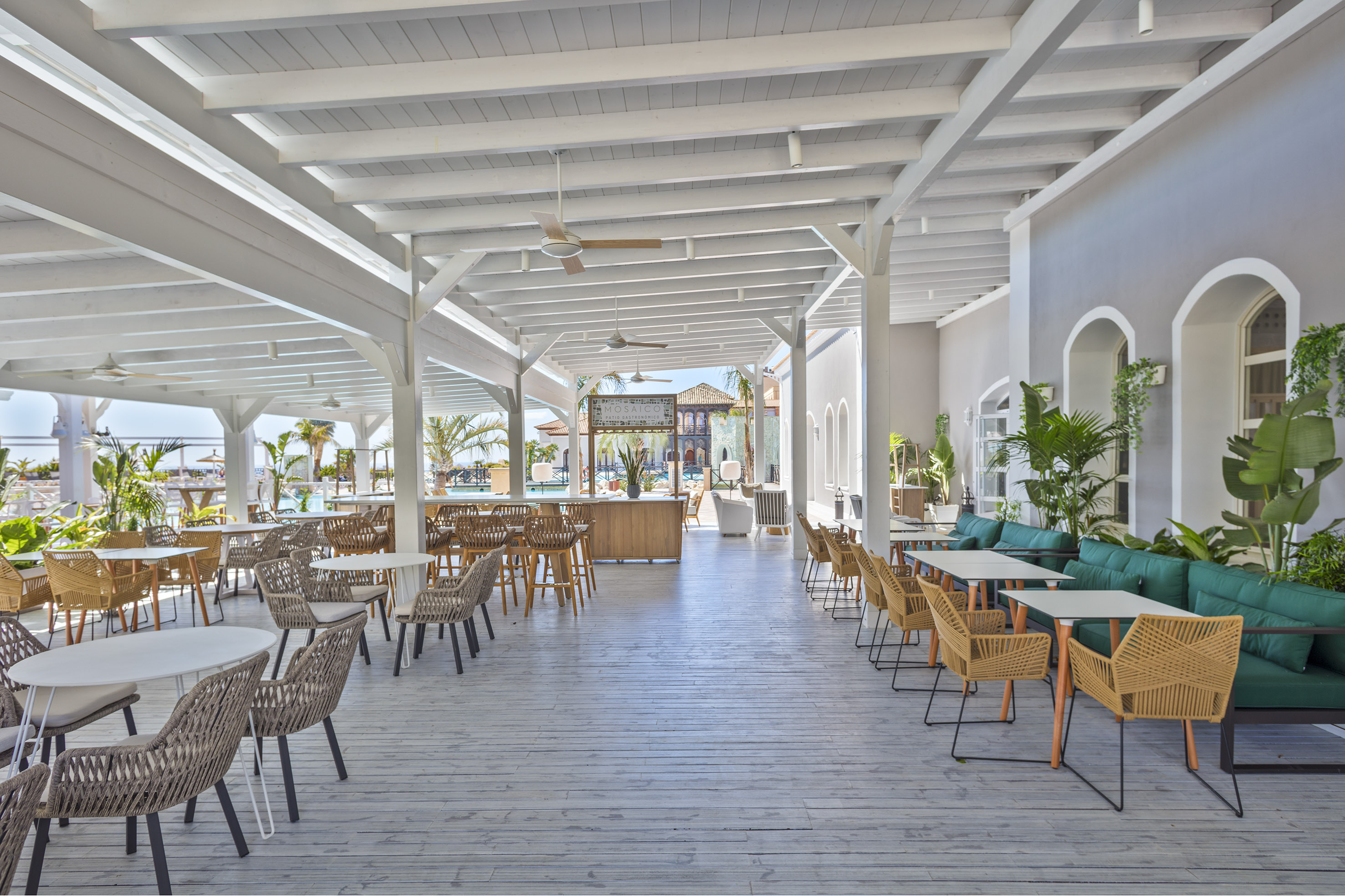 Modern outdoor restaurant patio with white wood, woven chairs, and tropical plants.
