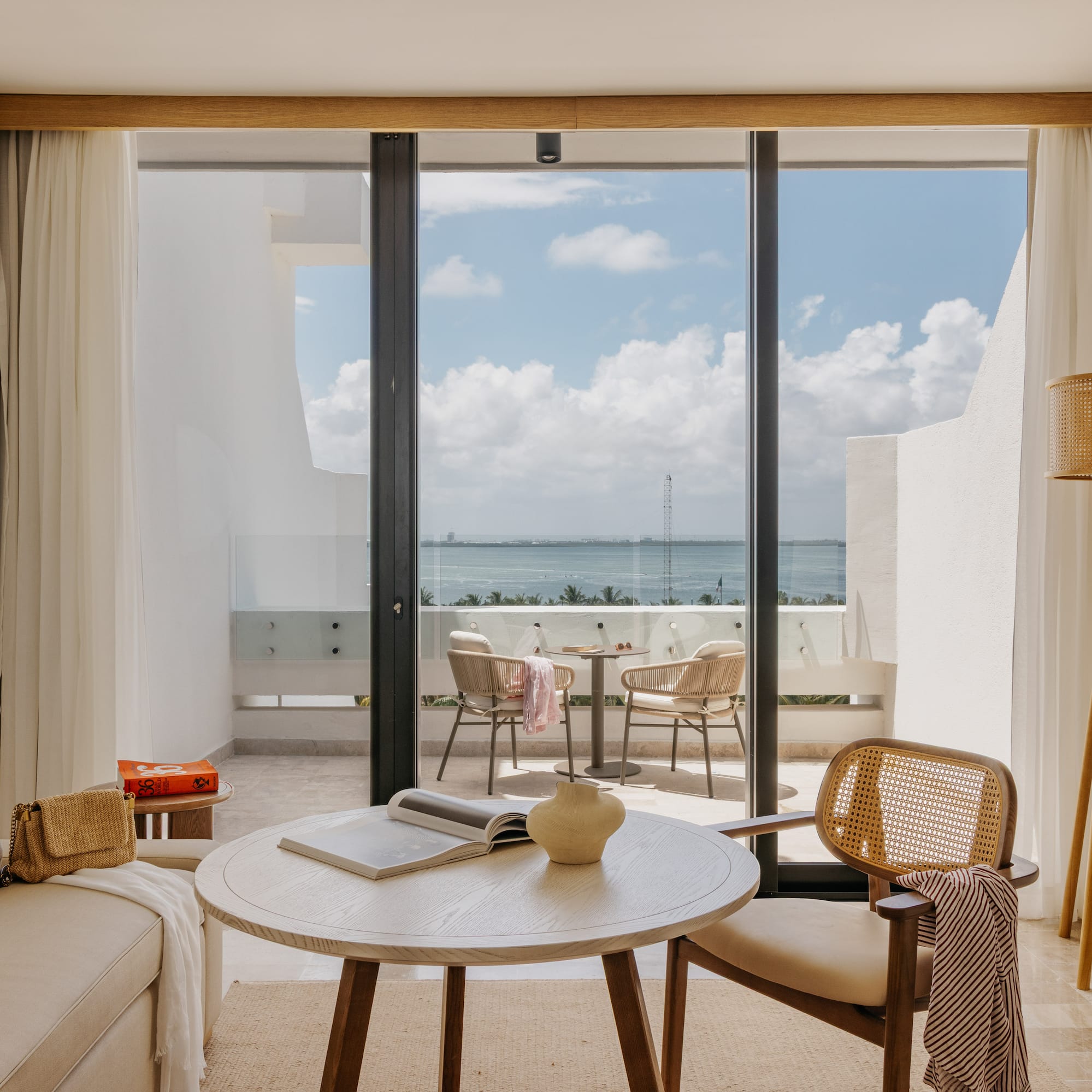 Hotel suite living room with ocean view balcony, modern and natural design.