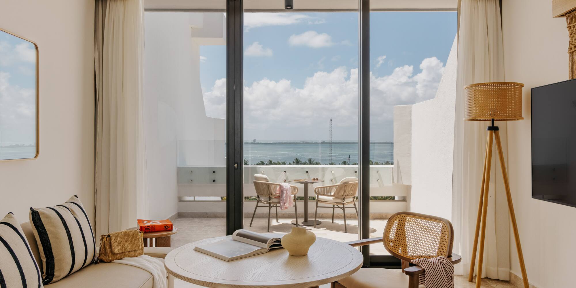 Hotel suite living room with ocean view balcony, modern and natural design.