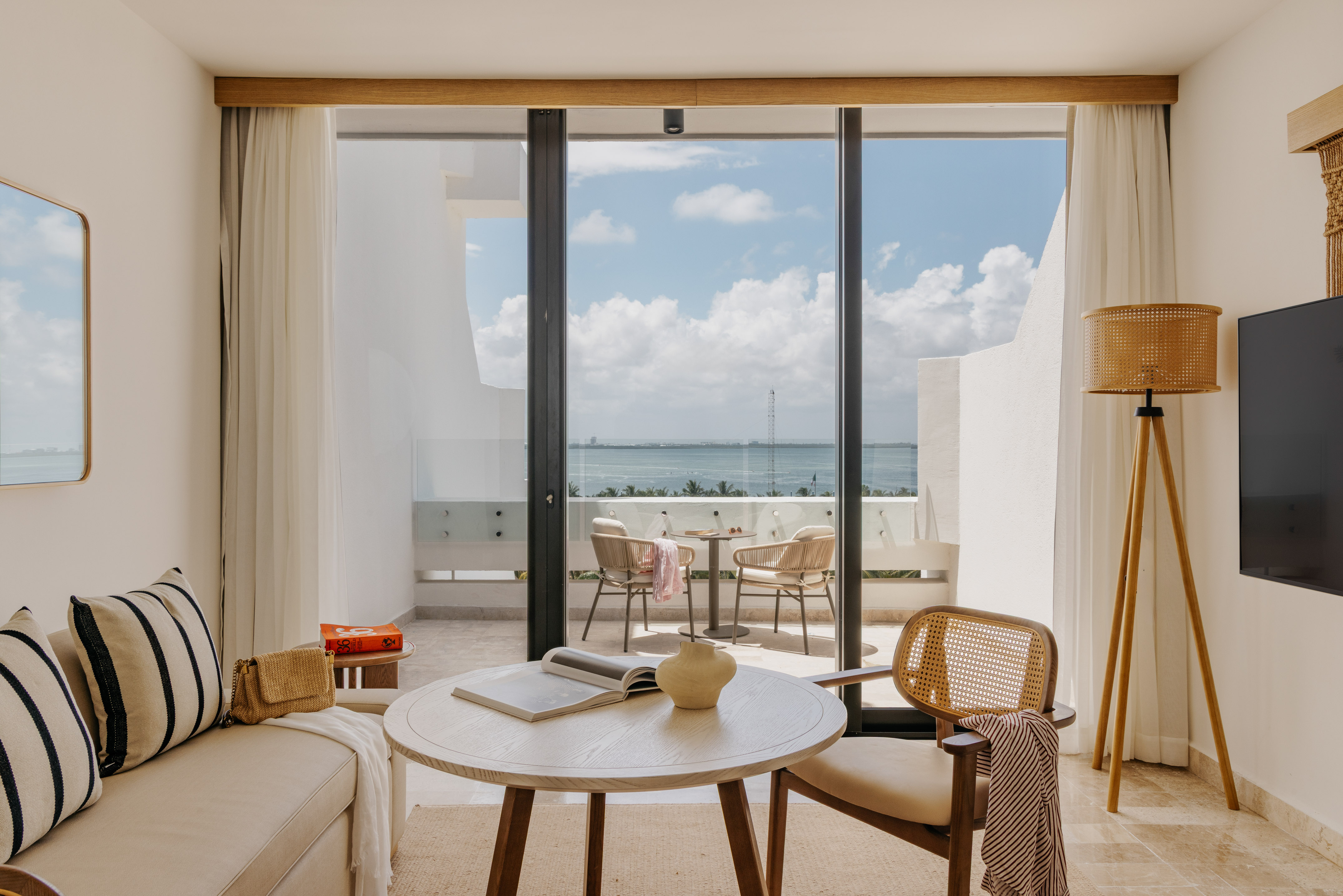 Hotel suite living room with ocean view balcony, modern and natural design.