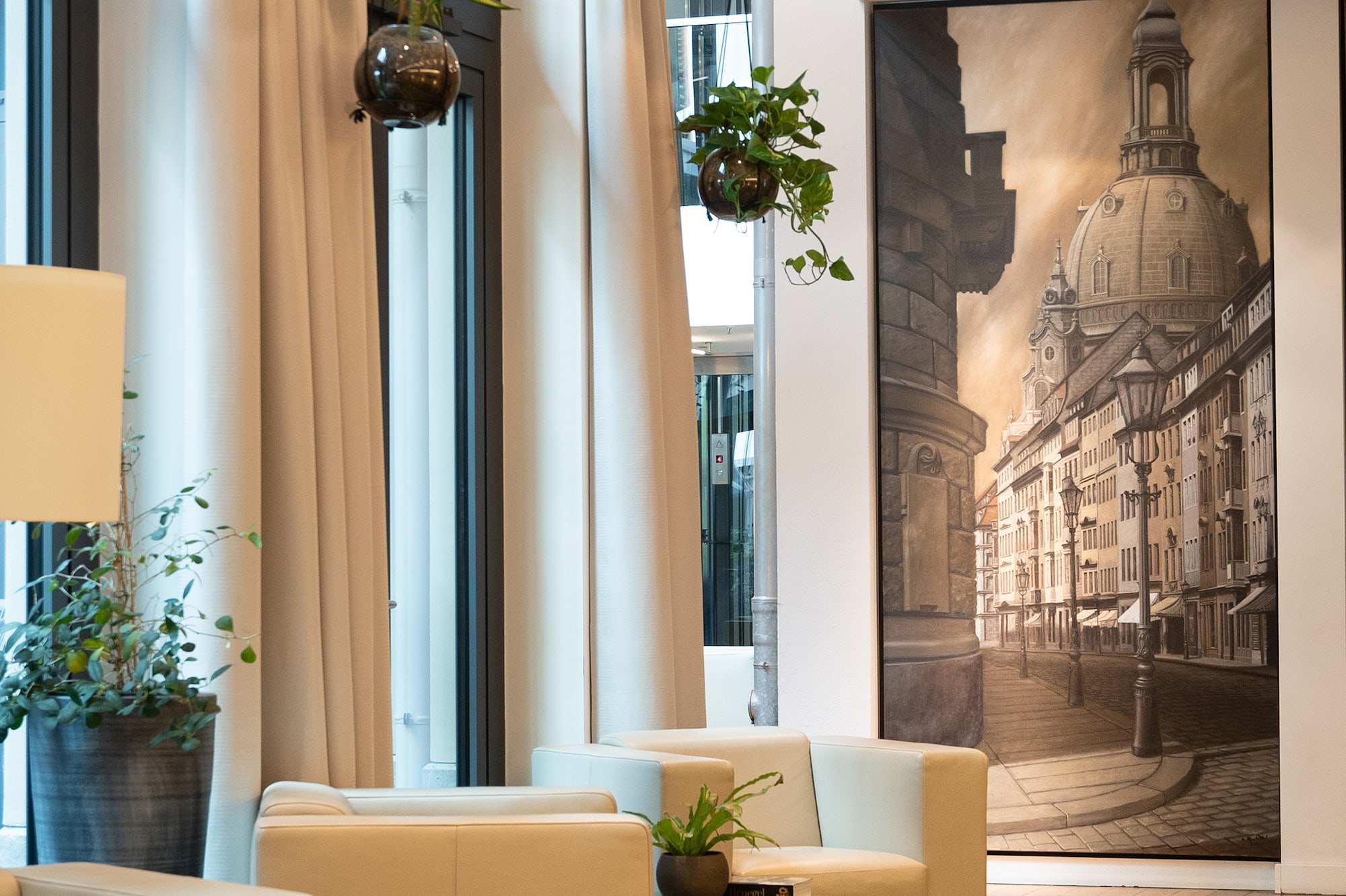 Modern lobby with cream seating, wood floor, potted plants, and large Dresden cityscape.