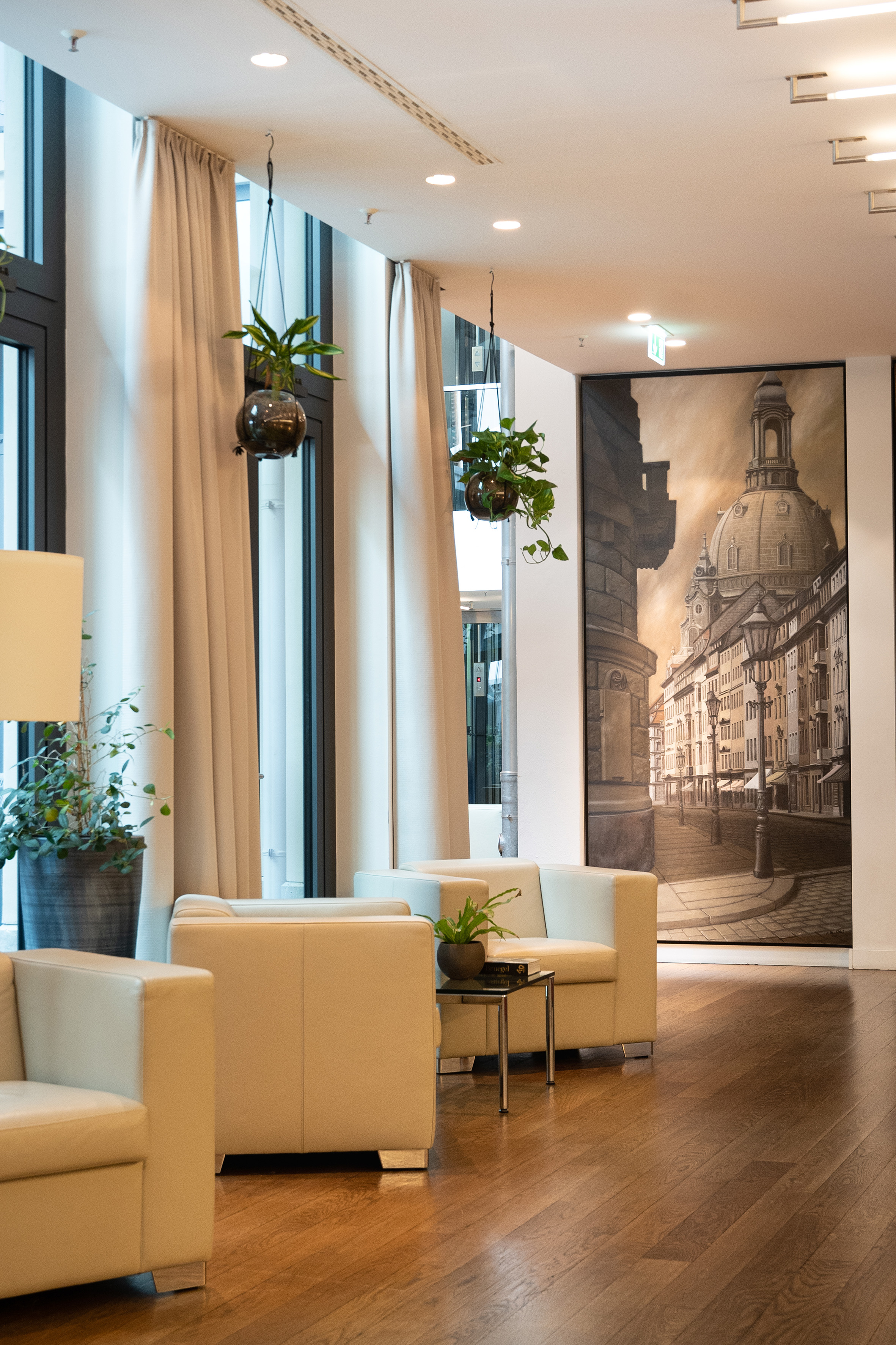 Modern lobby with cream seating, wood floor, potted plants, and large Dresden cityscape.