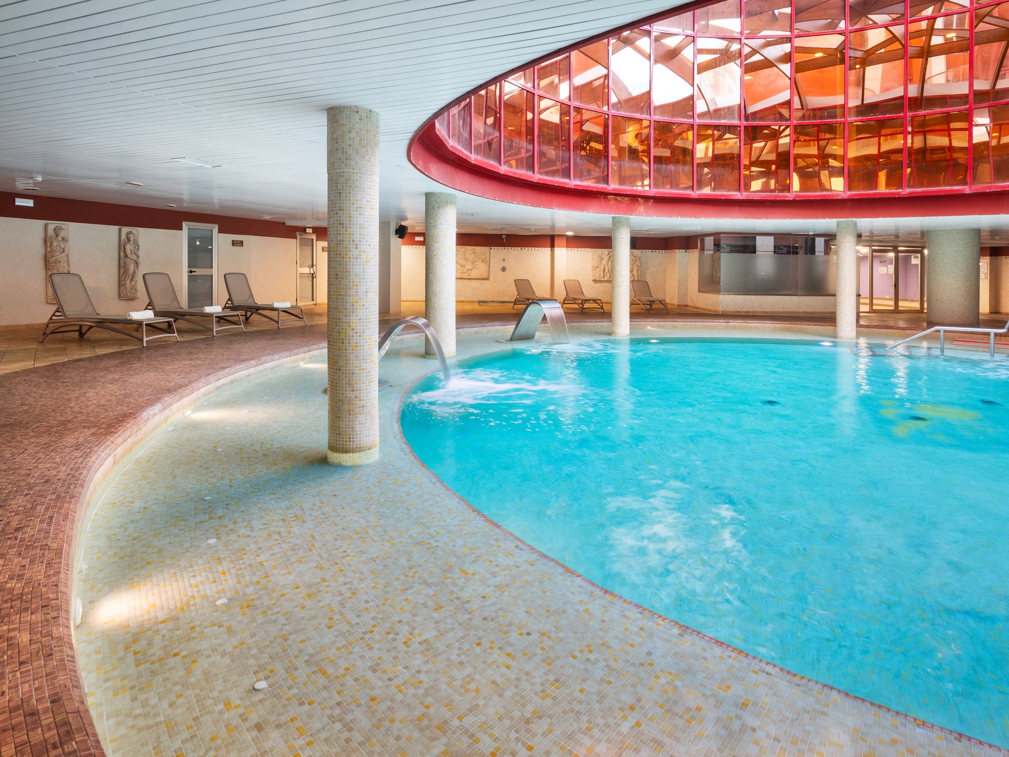 Indoor hotel spa pool with hydrotherapy jets, lounge seating, red glass dome.