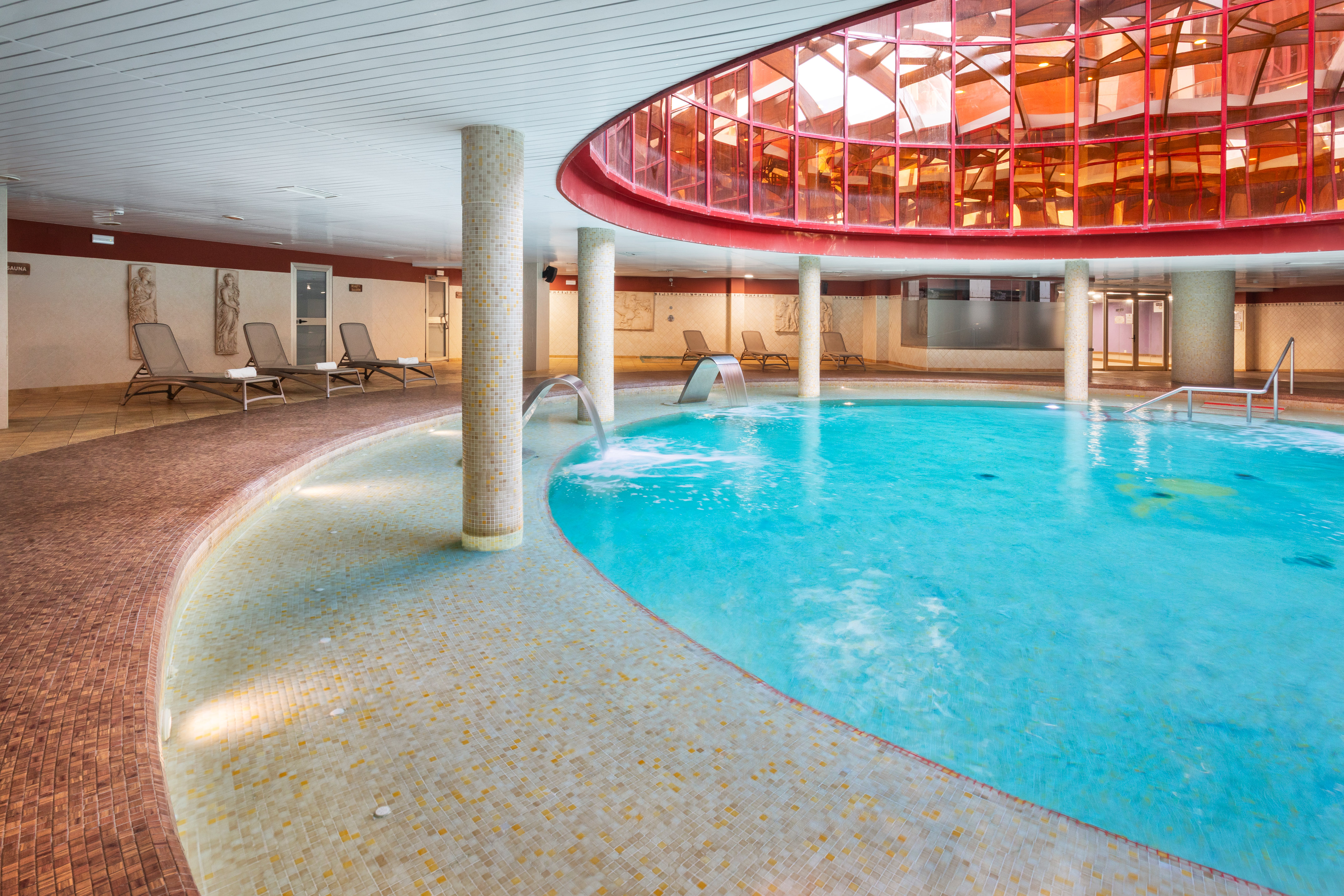 Indoor hotel spa pool with hydrotherapy jets, lounge seating, red glass dome.