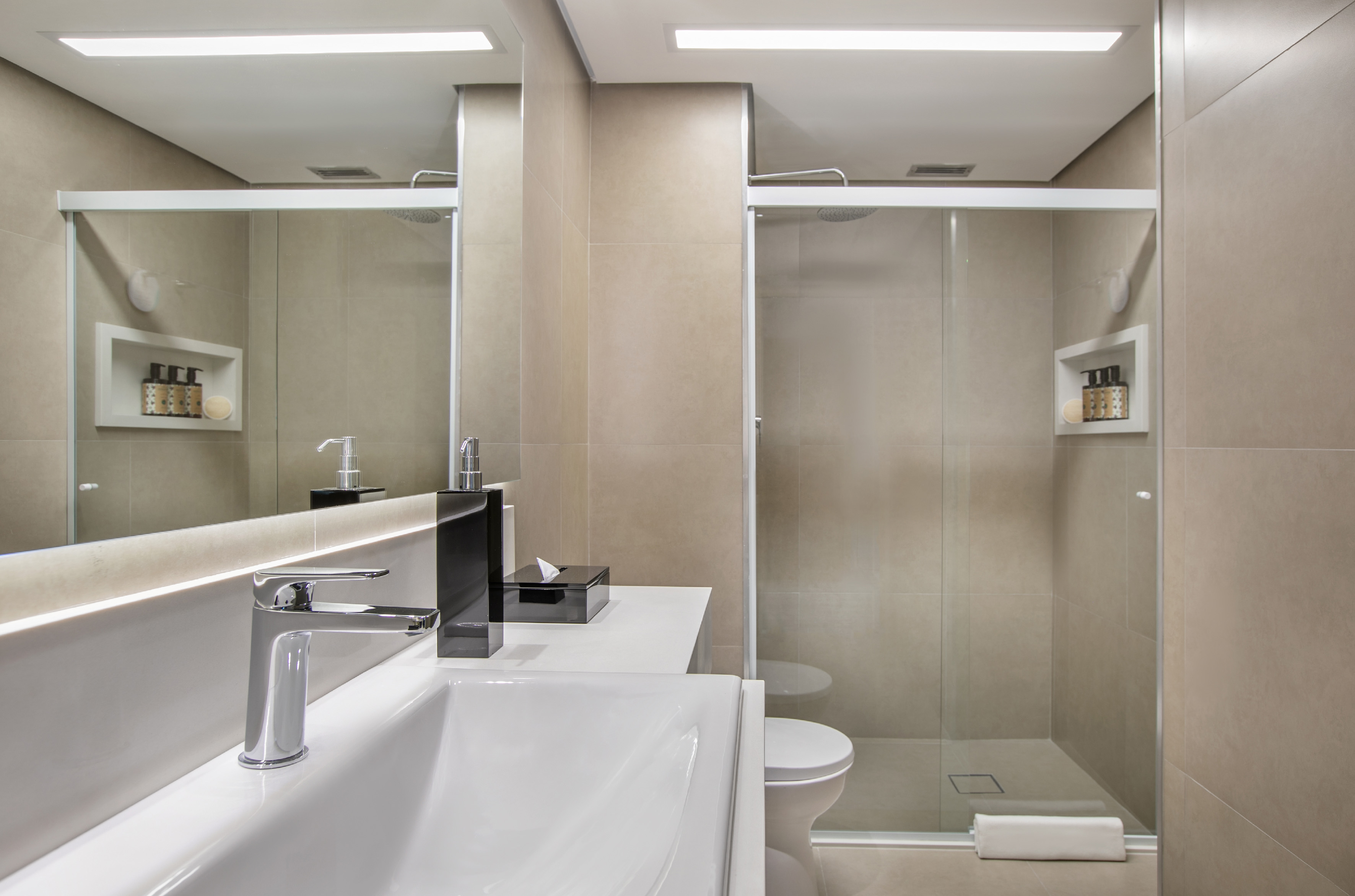 Modern beige bathroom with sink, backlit mirror, toilet, and glass shower.