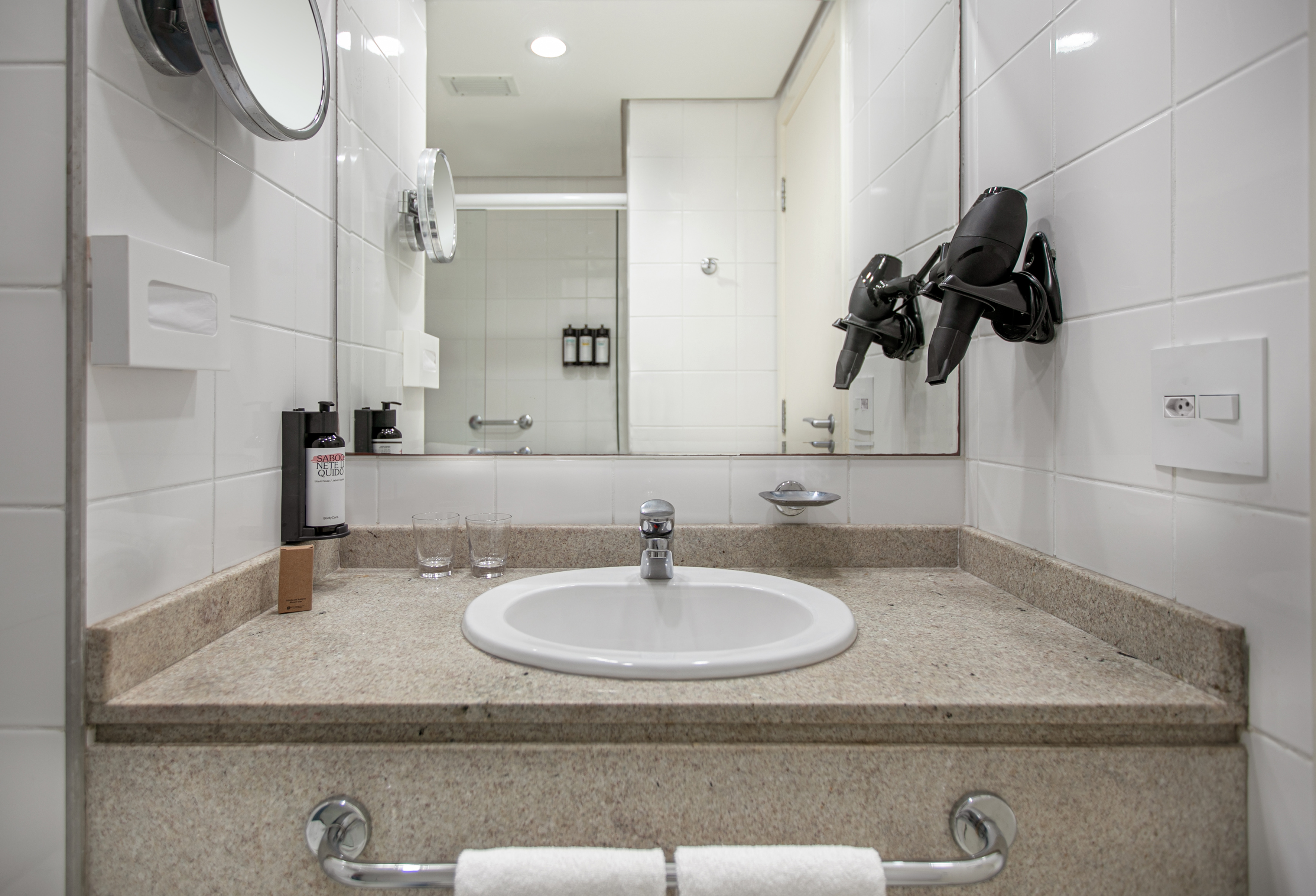 Hotel bathroom vanity with sink, mirror, hairdryer, and toiletries on granite counter.