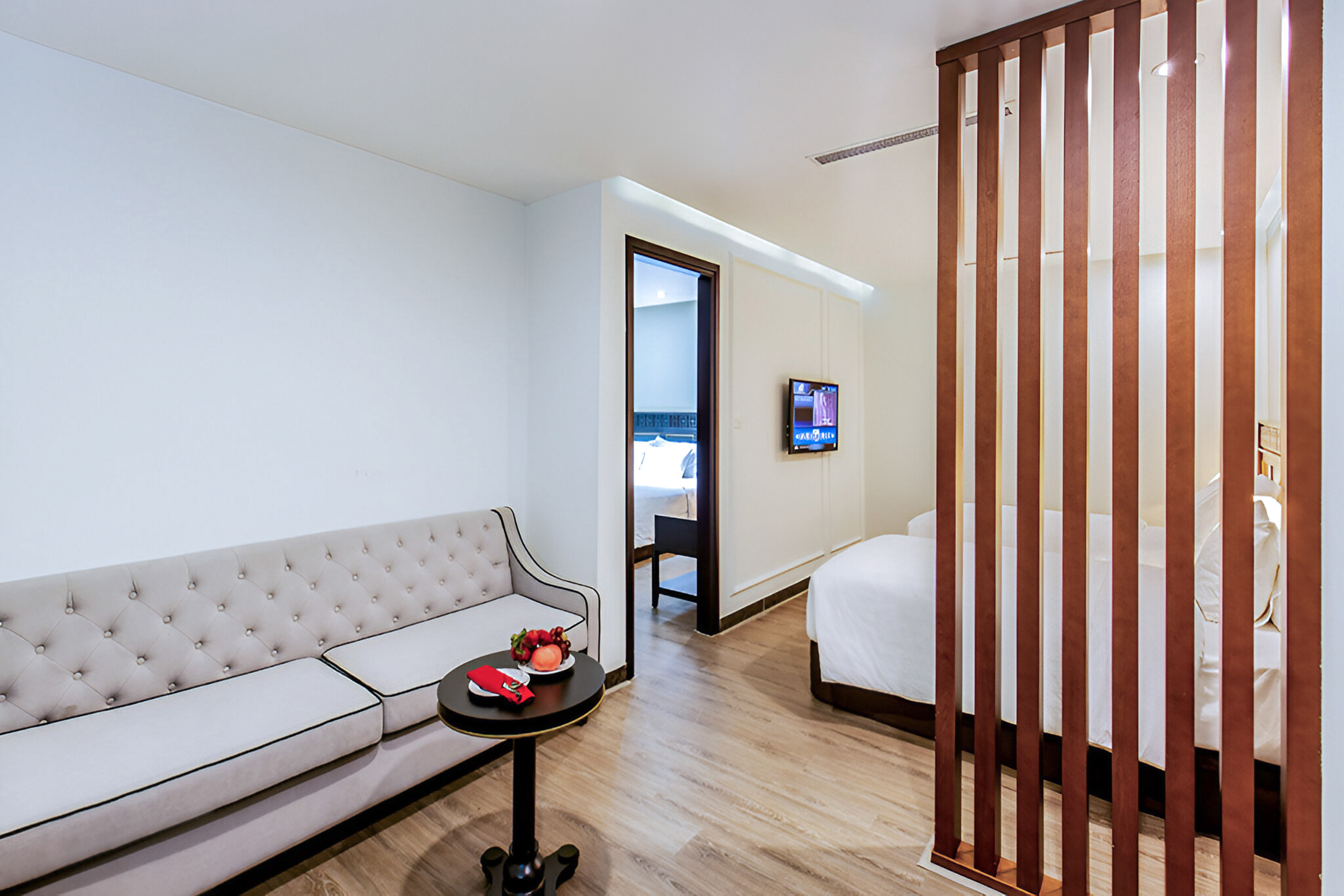 Modern hotel suite with gray sofa, fruit, and wooden partition to bedroom. - Family Room - Hotel Sapa Square Affiliated by Meliá, Sapa