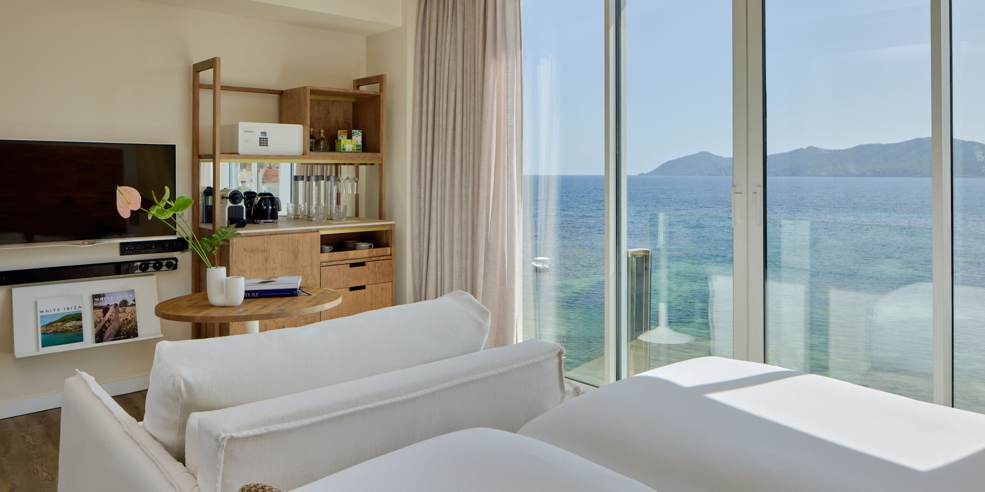 Luxury resort room with ocean view, modern bed, sofa, and wooden mini-bar.