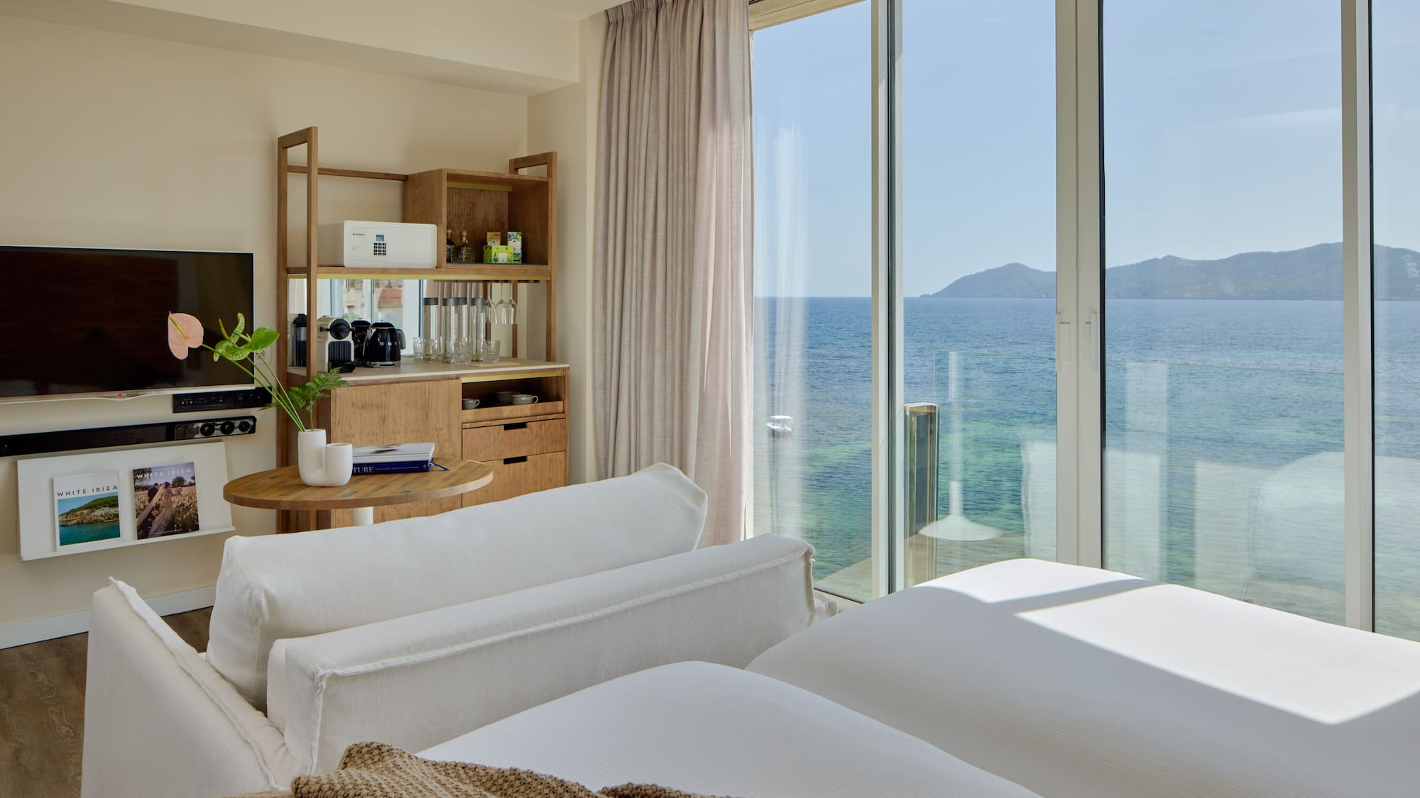 Luxury resort room with ocean view, modern bed, sofa, and wooden mini-bar.
