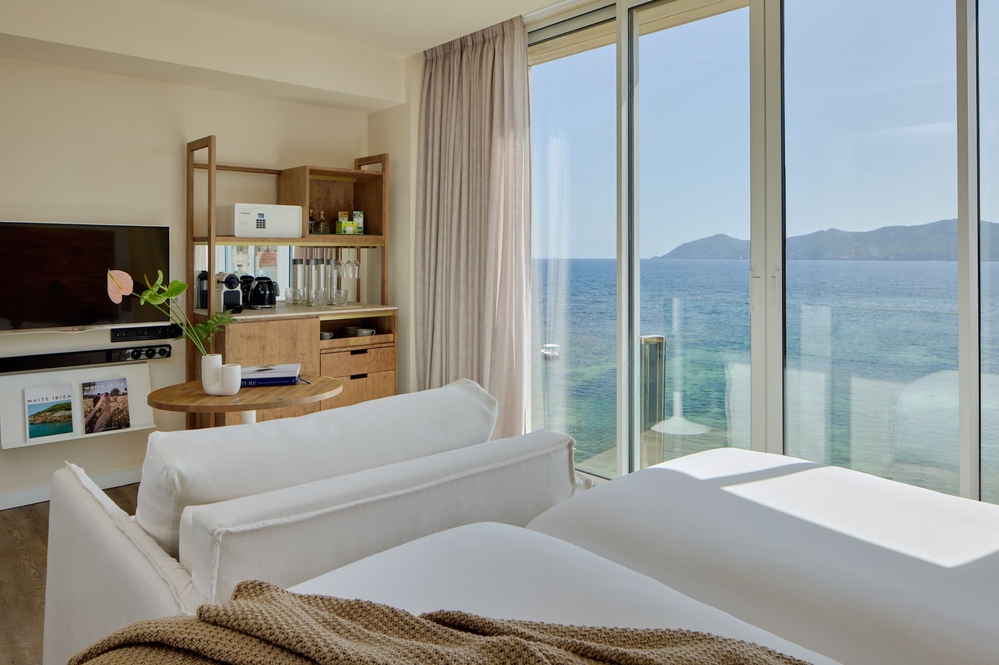Luxury resort room with ocean view, modern bed, sofa, and wooden mini-bar.