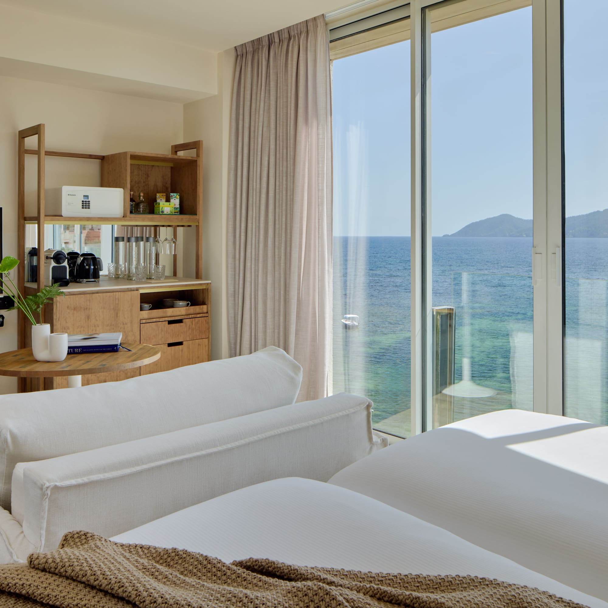Luxury resort room with ocean view, modern bed, sofa, and wooden mini-bar.