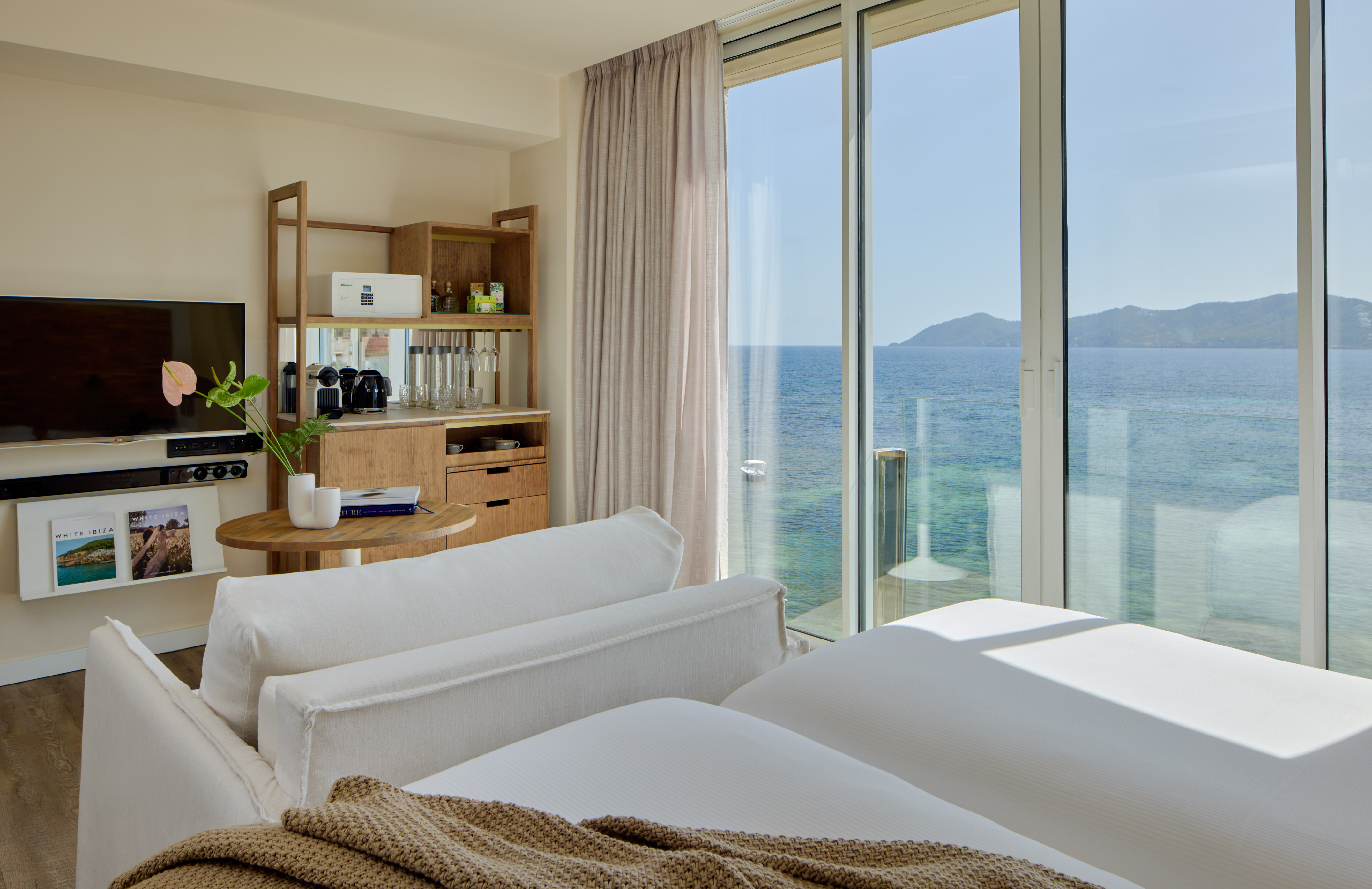 Luxury resort room with ocean view, modern bed, sofa, and wooden mini-bar.