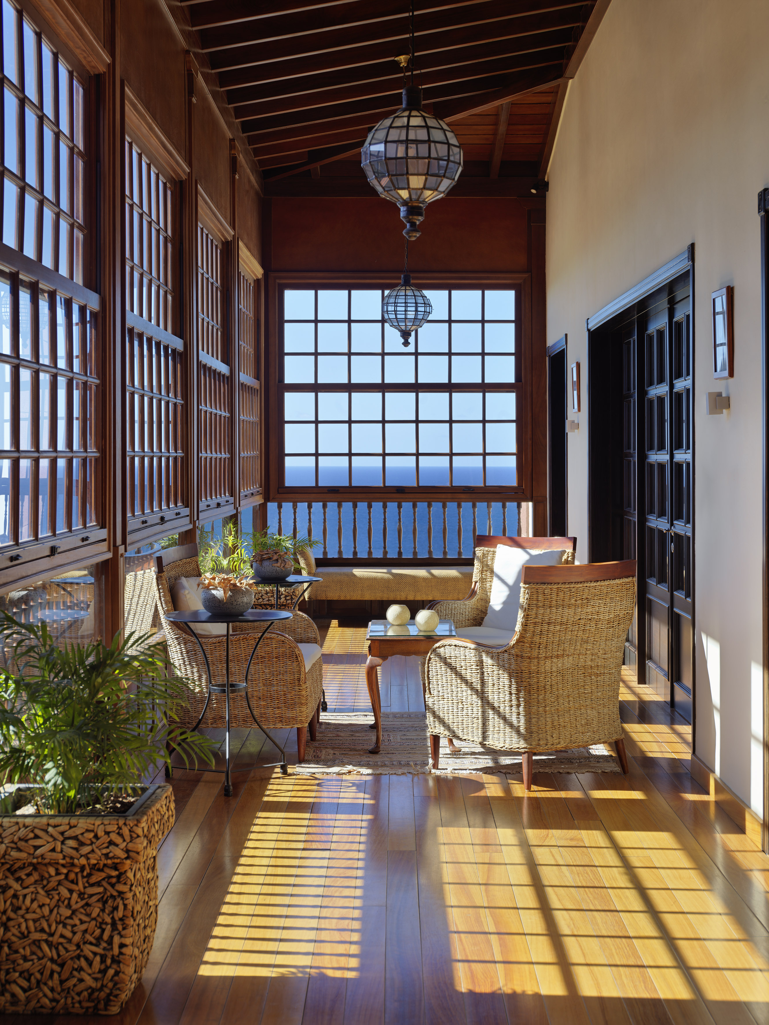 Sunny wooden sunroom with wicker chairs, sea view windows, and patterned shadows.