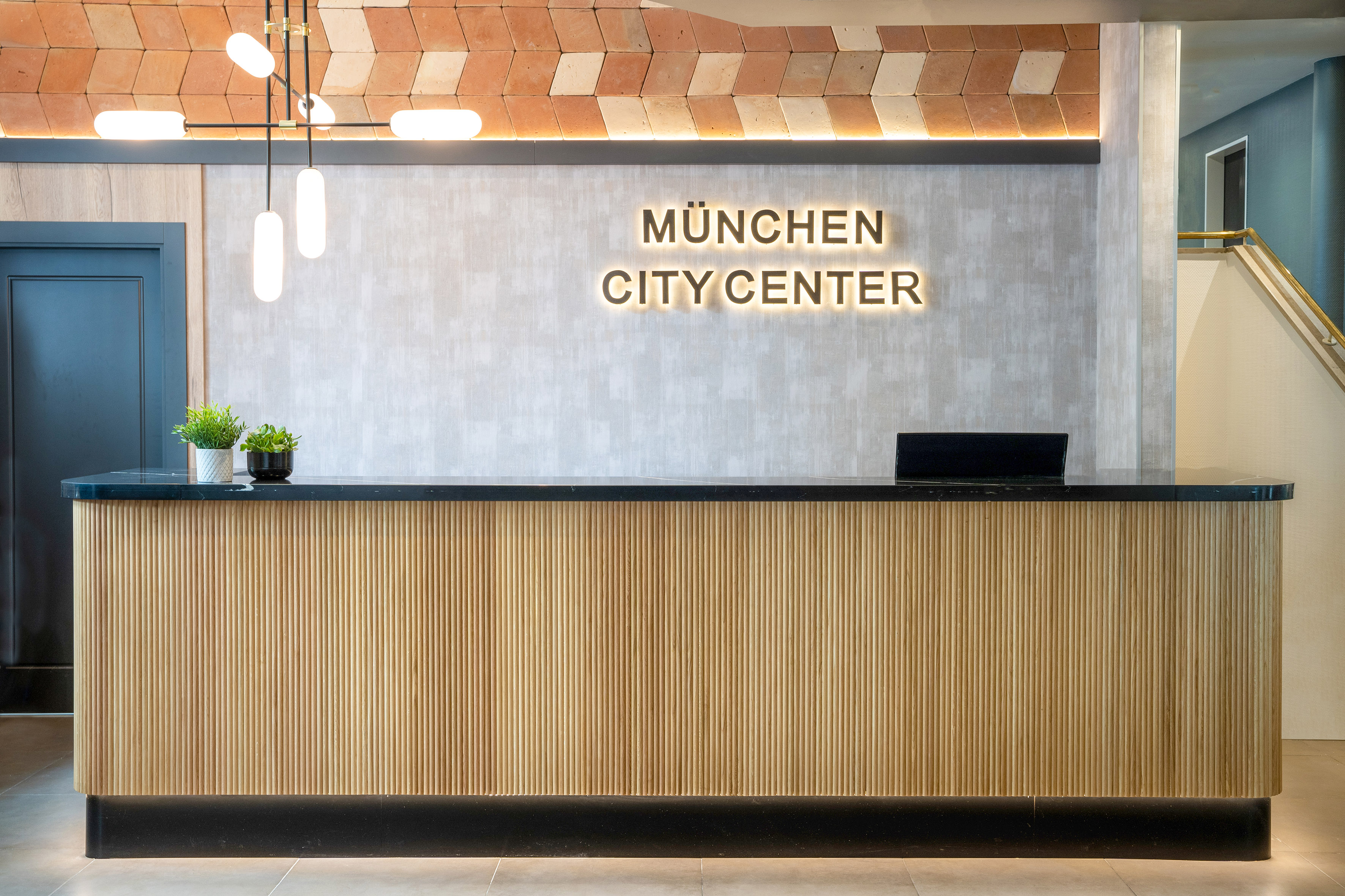 Modern hotel reception desk with "München City Center" glowing sign.