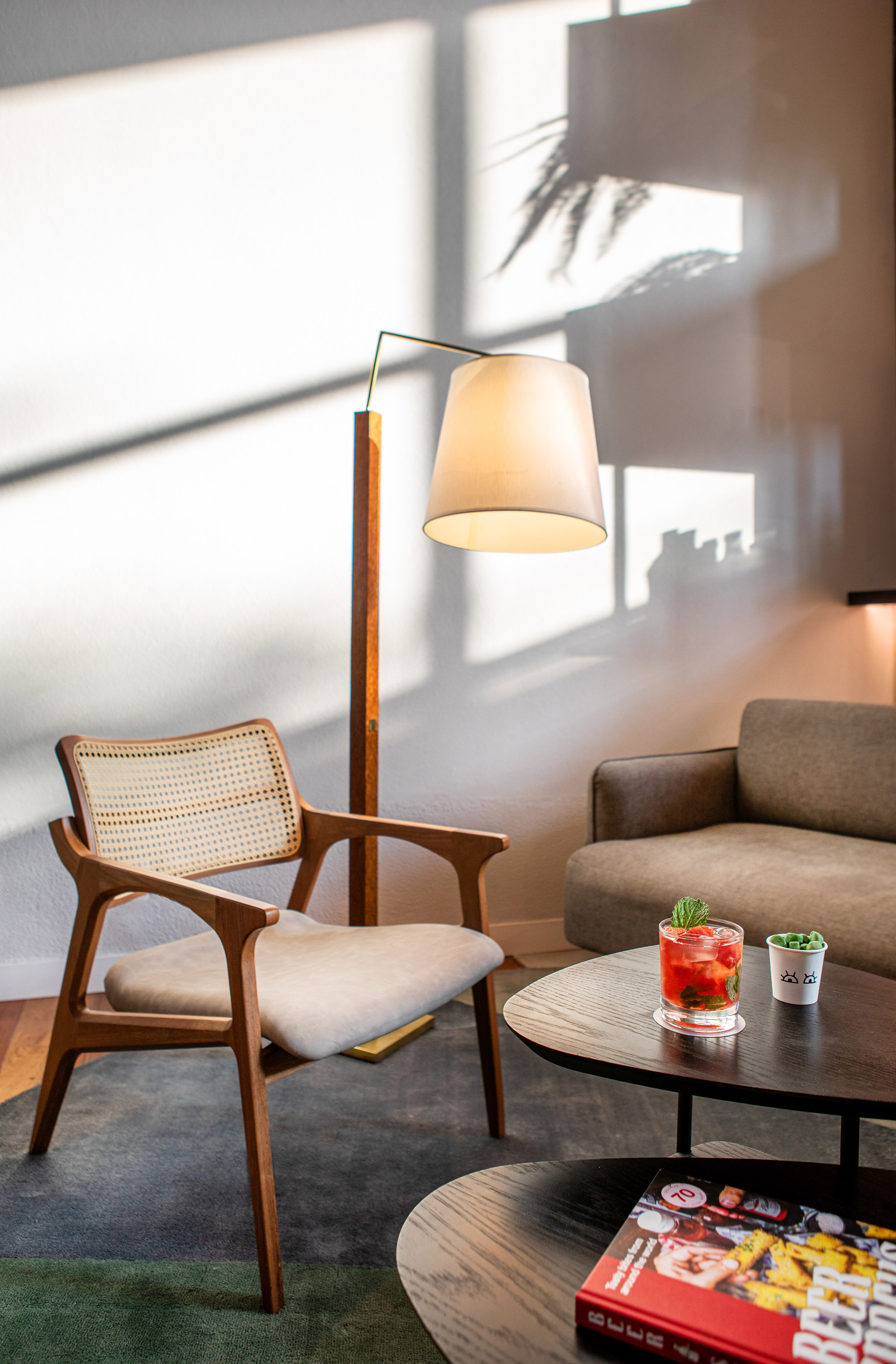 Modern lounge interior with wooden armchair, floor lamp, sofa, and cocktail.
